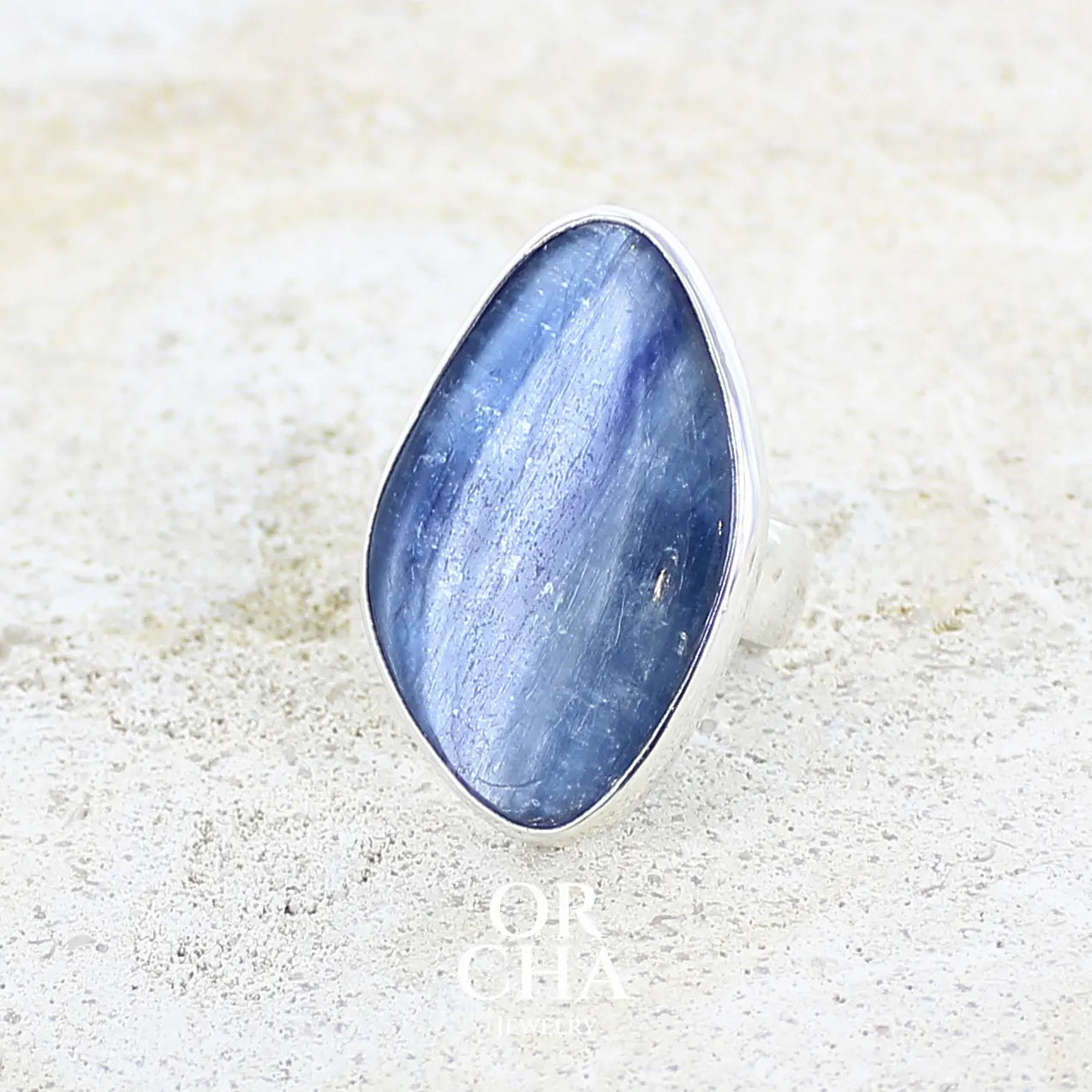 Profil gauche d'une bague pour femme en argent massif sertie d'un cabochon de cyanite de couleur bleu jean nacré. Pierre translucide à inclusions. Bijou unique réalisée en taille 54 par Orcha Jewelry