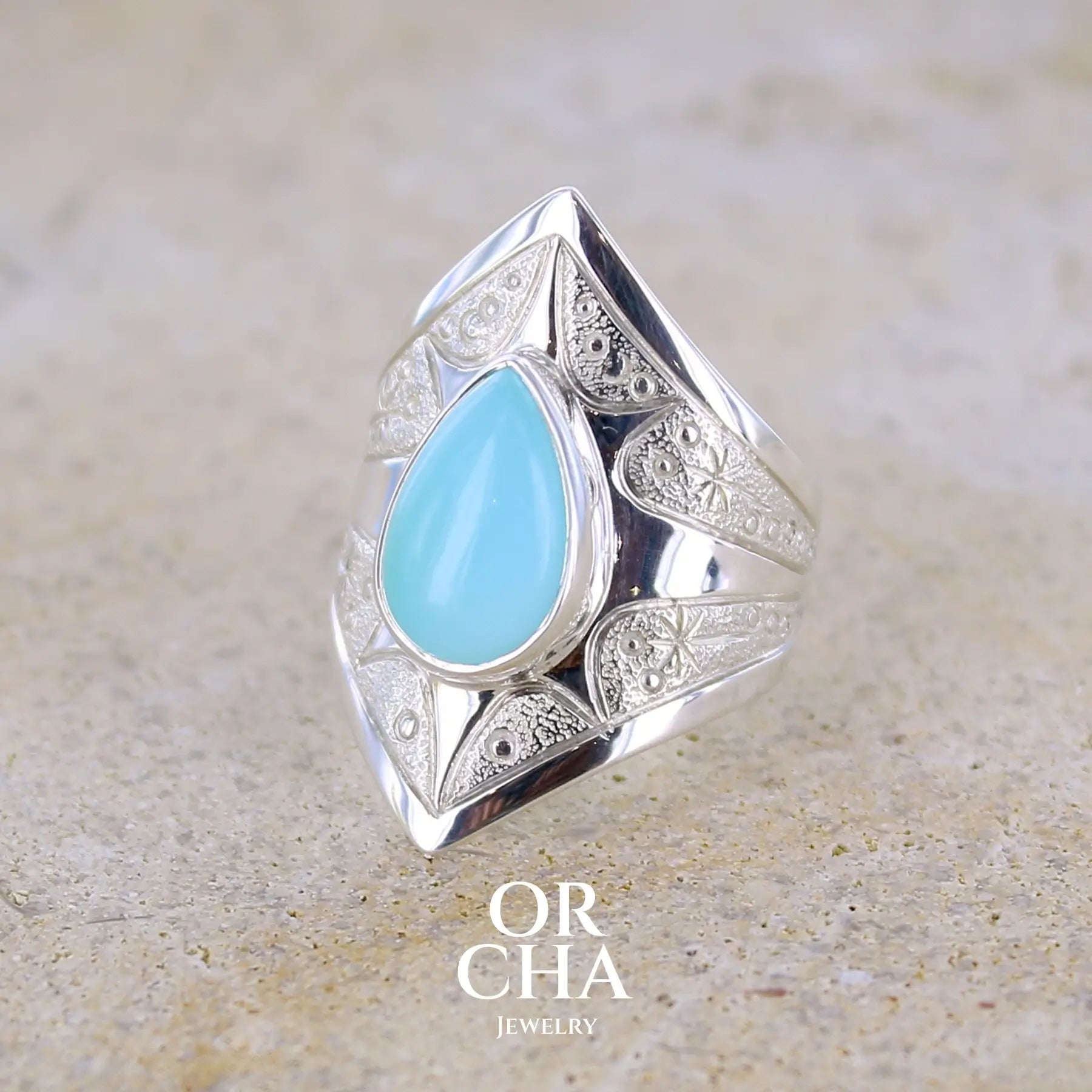 Profil gauche d'une bague pour femme en argent massif sculptées d'étoiles et autres corps célestes sertie d'une Opale bleue du Pérou. Pierre cabochon en forme de goutte, pierre naturelle de couleur bleu ciel ciel, bleu turquoise. Pierre naturelle de qualité opaque. Taille 51. Bijoux unique, éthique et durable présenté dans un coffret de notre marque, prêt à offrir. Livraison offerte, certificat d'authenticité, service client.