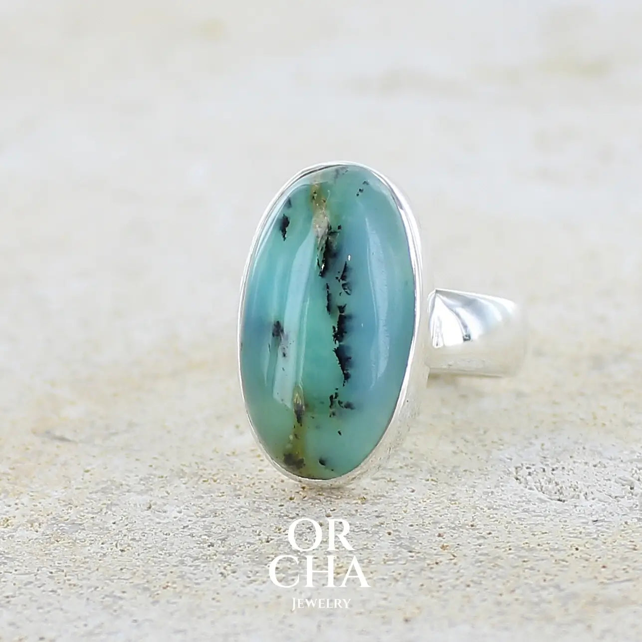 Profil gauche d'une bague en argent massif, sertie d'un cabochon ovale d'opale bleue du Pérou de couleur bleu foncé à inclusions de dendrites paysages noires et de roche mère jaune. Pierre naturelle opaque et translucide. Bijoux unique réalisé en taille 52 par Orcha jewelry