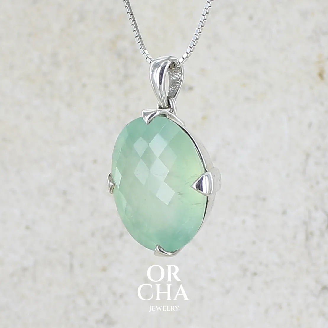 Profil gauche d un pendentif ovale en argent massif, serti d'un cabochon facetté de préhnite de couleur verte pastel. Pierre de qualité translucide comportant des inclusions. Bijoux unique par Orcha Jewelry