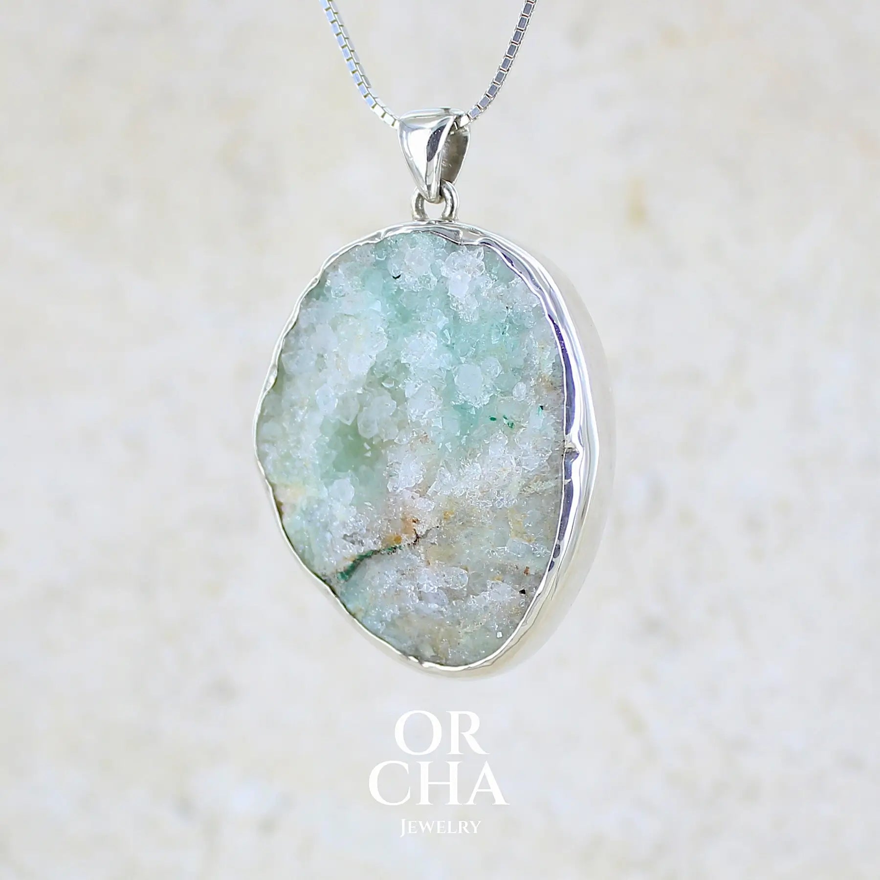 Profil gauche d'un pendentif en argent massif serti d'un magnifique gemsilica druze: chrysocolle silicifiée recouverte de fins cristaux de quartz scintillant. Pierre de qualité opaque brute de forme ovale. Pierre naturelle originaire du Mexique de couleur verte bleutée claire.
