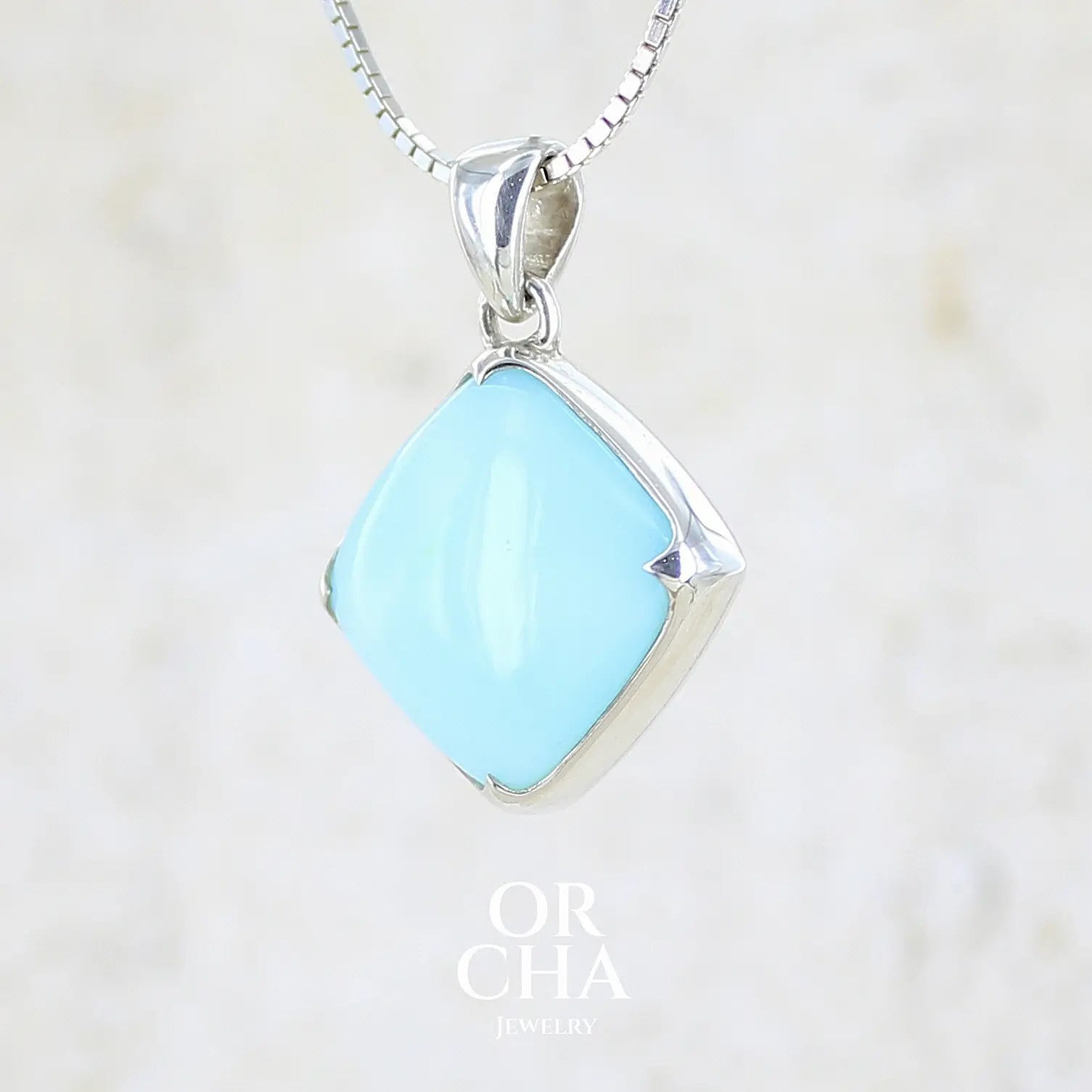 profil gauche d'un pendentif en argent massif, sertie d'un cabochon d'opale bleue du Pérou de couleur bleu ciel clair. Pierre de forme carrée. Pierre opaque. Bijoux unique, éthique et durable présenté dans un coffret de notre marque, prêt à offrir. Livraison offerte, certificat d'authenticité, service client.