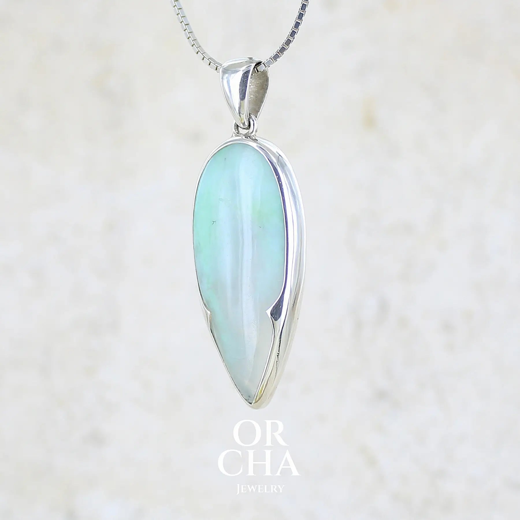 profil gauche d'un pendentif pour femme et homme en argent massif, sertie d'un cabochon d'opale bleue du Pérou de couleur verte bleutée. Pierre en forme de goutte inversée. Pierre opaque et translucide. Bijoux unique, éthique et durable présenté dans un coffret de notre marque, prêt à offrir. Livraison offerte, certificat d'authenticité, service client.