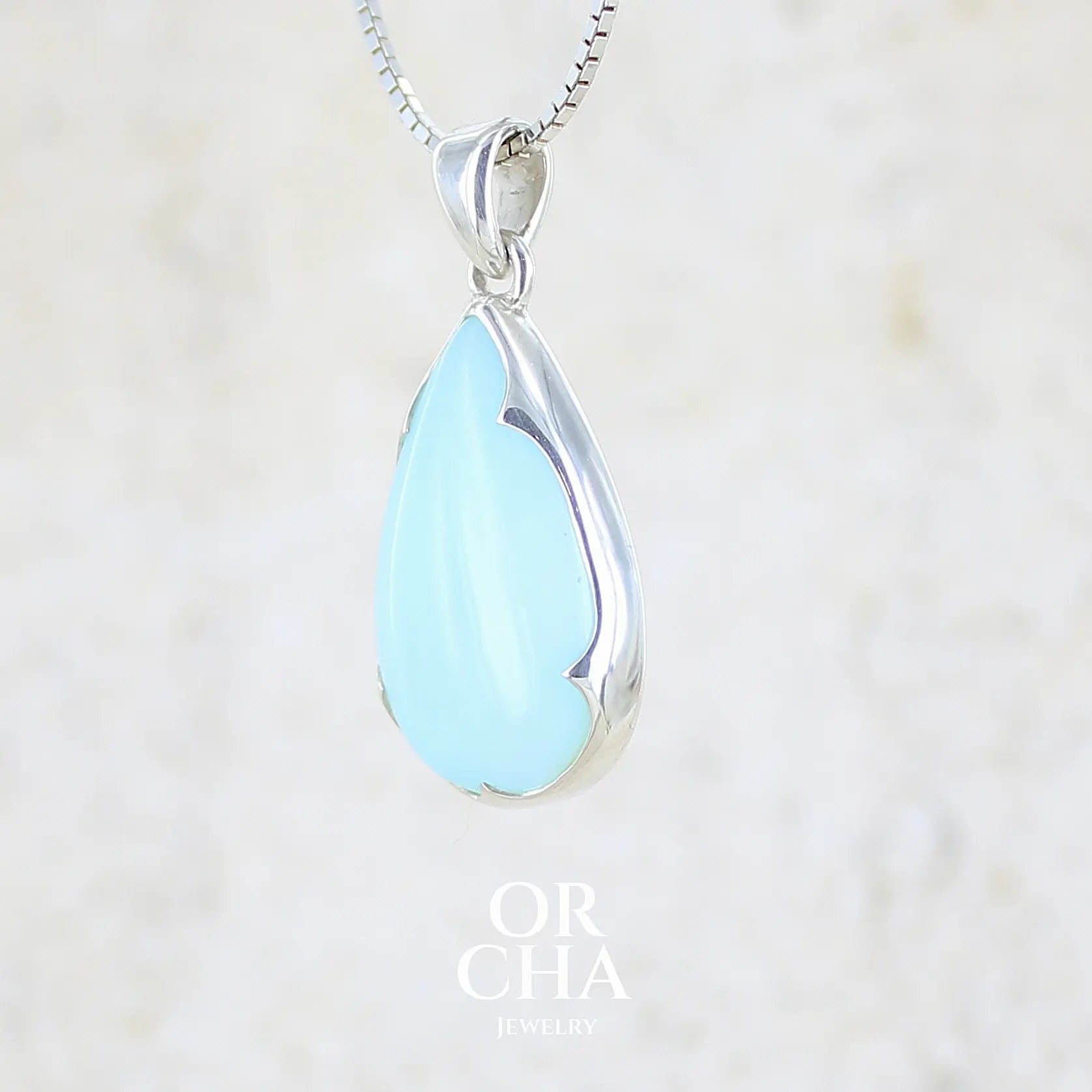 profil gauche d'un pendentif pour femme en argent massif, sertie d'un cabochon d'opale bleue du Pérou de couleur bleu ciel clair. Pierre en forme de goutte. Pierre opaque. Bijoux unique, éthique et durable présenté dans un coffret de notre marque, prêt à offrir. Livraison offerte, certificat d'authenticité, service client.