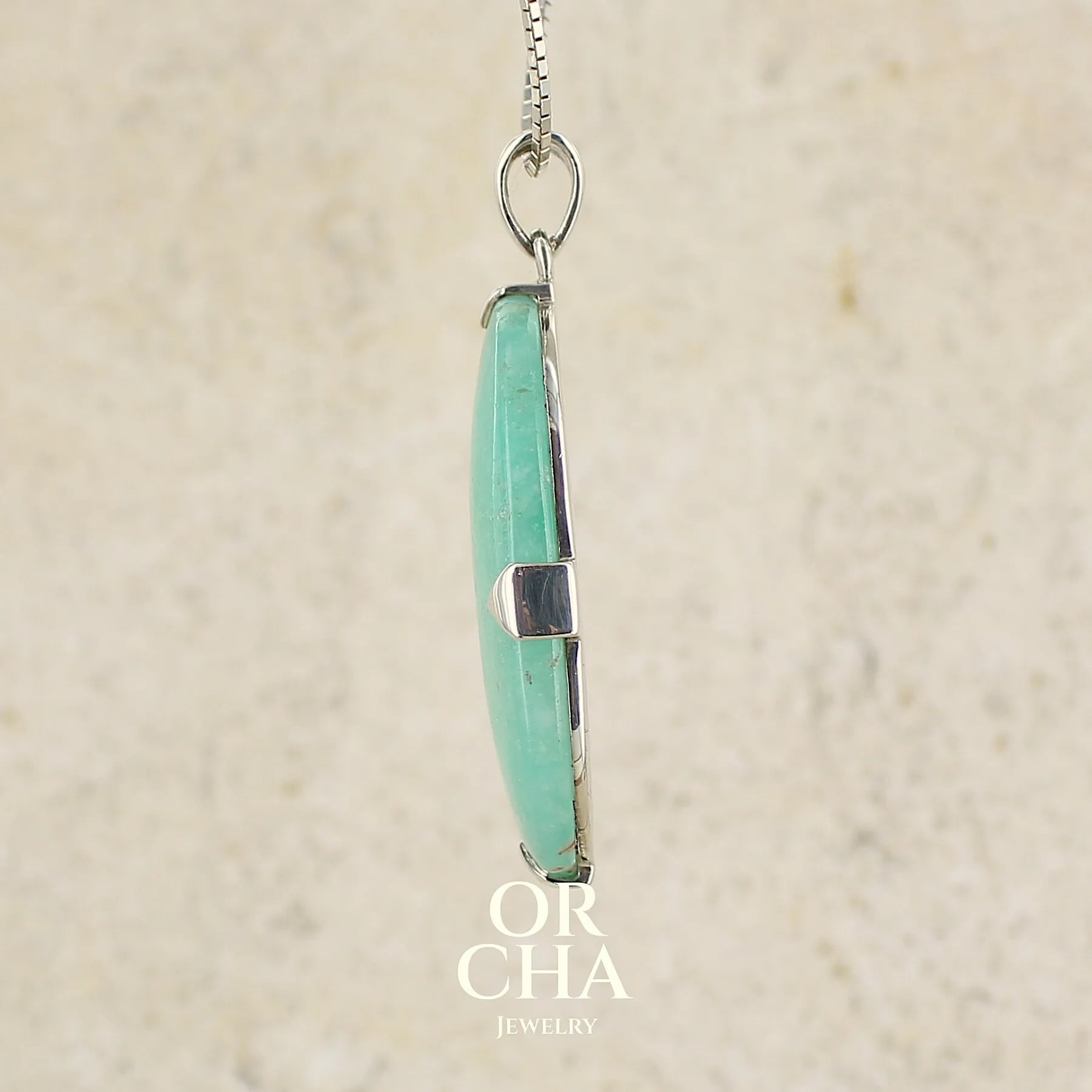 profil d'un pendentif ovale en argent massif, serti d'un cabochon de calcédoine de couleur bleue verte. Pierre de qualité translucide comportant des inclusions paysages blanches. Bijoux unique par Orcha Jewelry