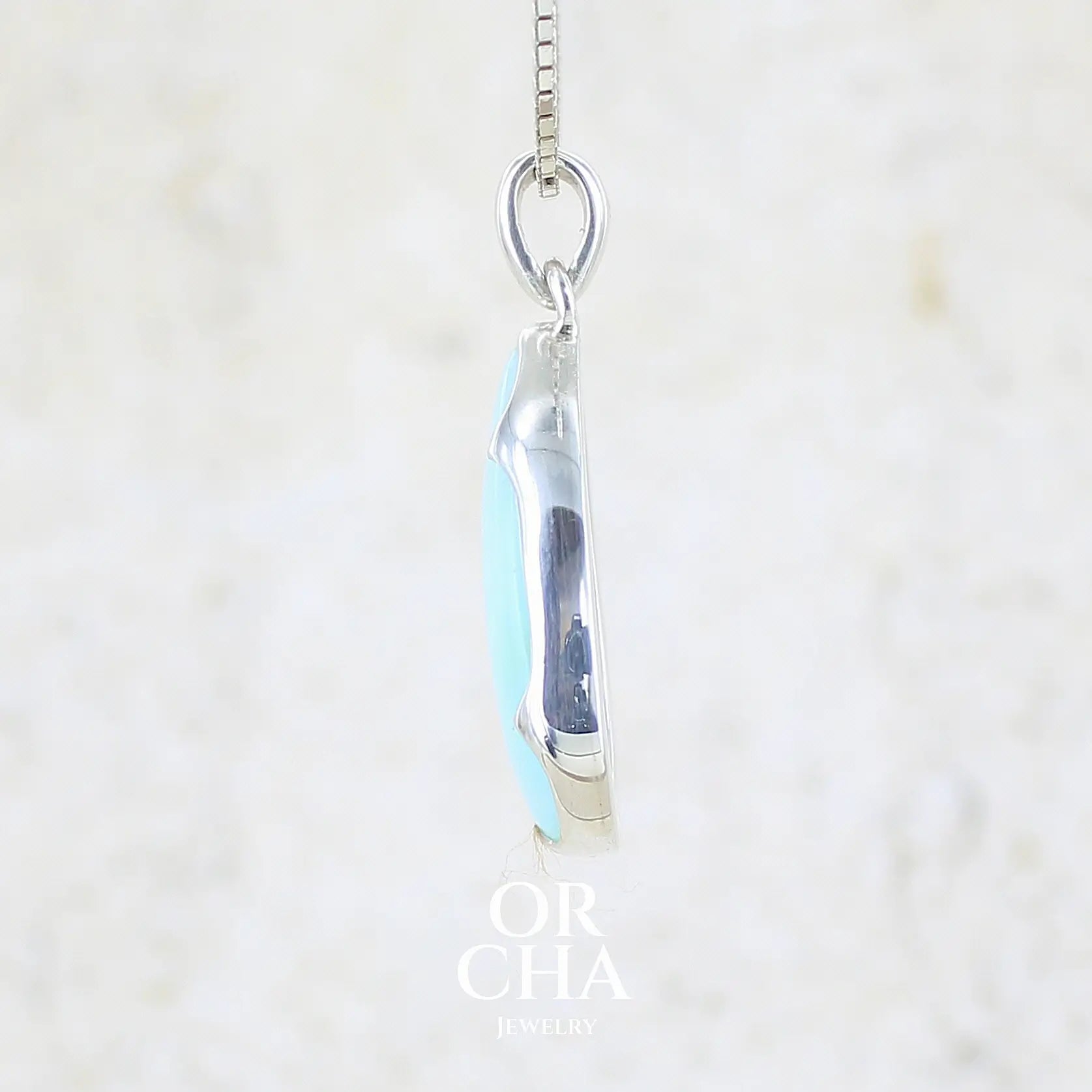 détail du sertissage d'un pendentif en argent massif, sertie d'un cabochon d'opale bleue du Pérou de couleur bleu ciel clair. Pierre en forme de goutte. Pierre opaque et translucide. Bijoux unique, éthique et durable présenté dans un coffret de notre marque, prêt à offrir. Livraison offerte, certificat d'authenticité, service client.