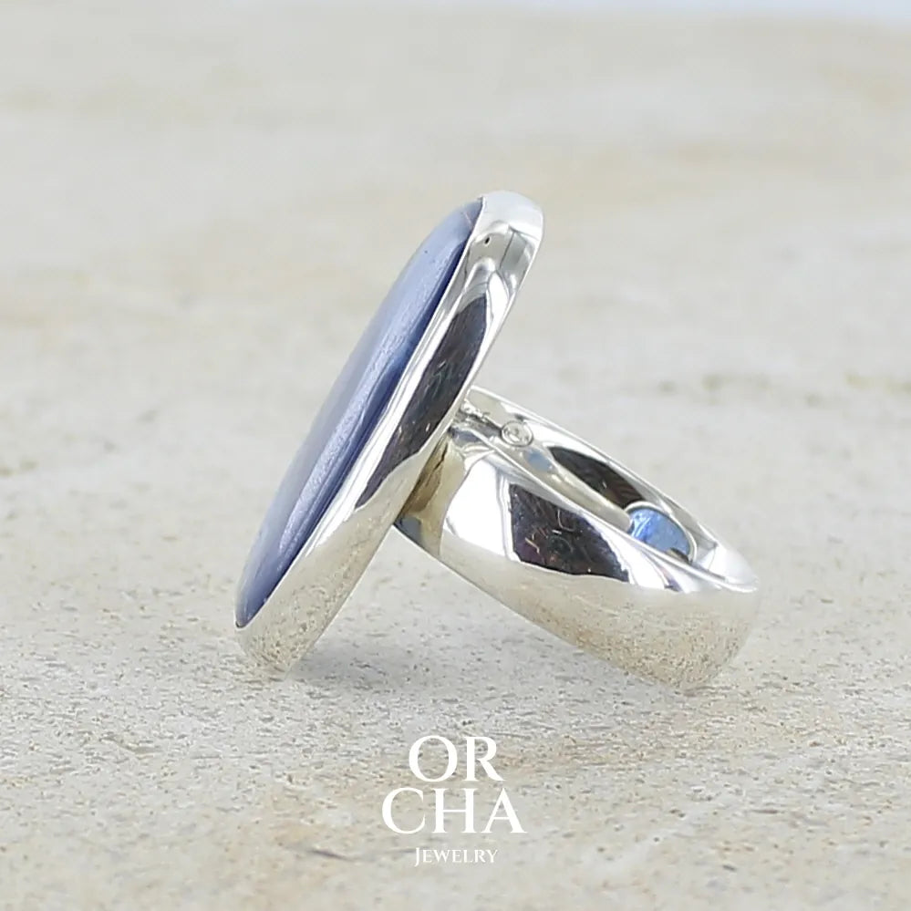 détail du sertissage d'une bague pour femme en argent massif, sertie d'un cabochon de cyanite de couleur bleue denim. Pierre transparente de forme ovale. Bijou unique réalisée en taille 52 par Orchajewelry