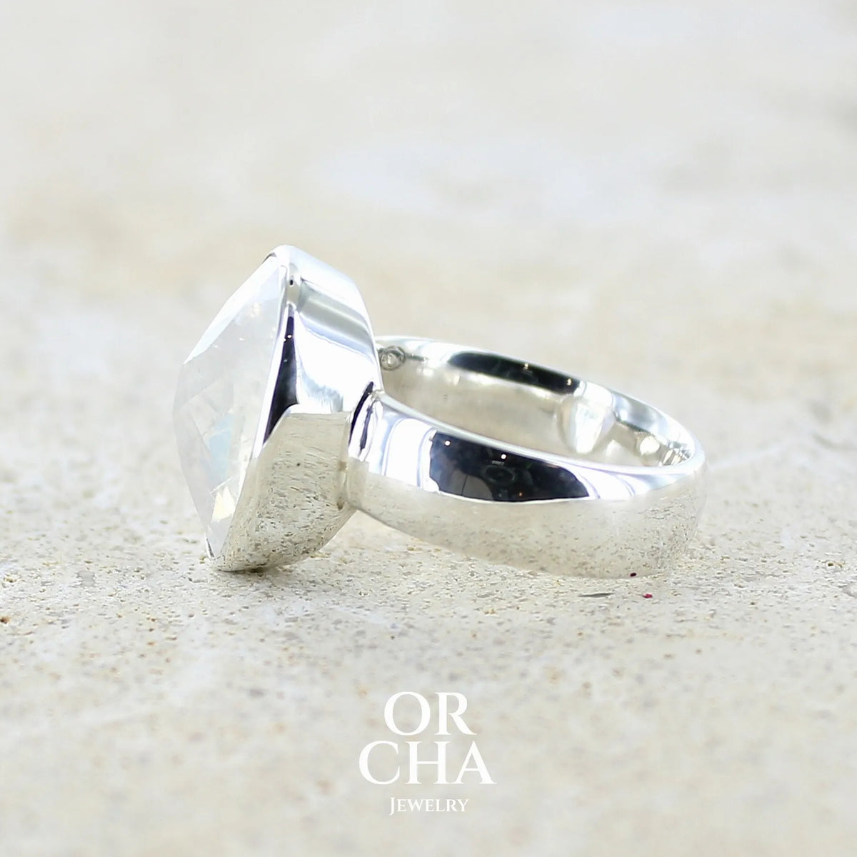Détail du sertissage d'une Bague cocktail pour femme en argent massif 925 sertie d'une Labradorite blanche taillée de 6,7 carats incolore aux reflets bleutés et arc en ciel. Pierre transparente avec inclusions. Bijoux unique réalisée en taille 57 par Orchajewelry
