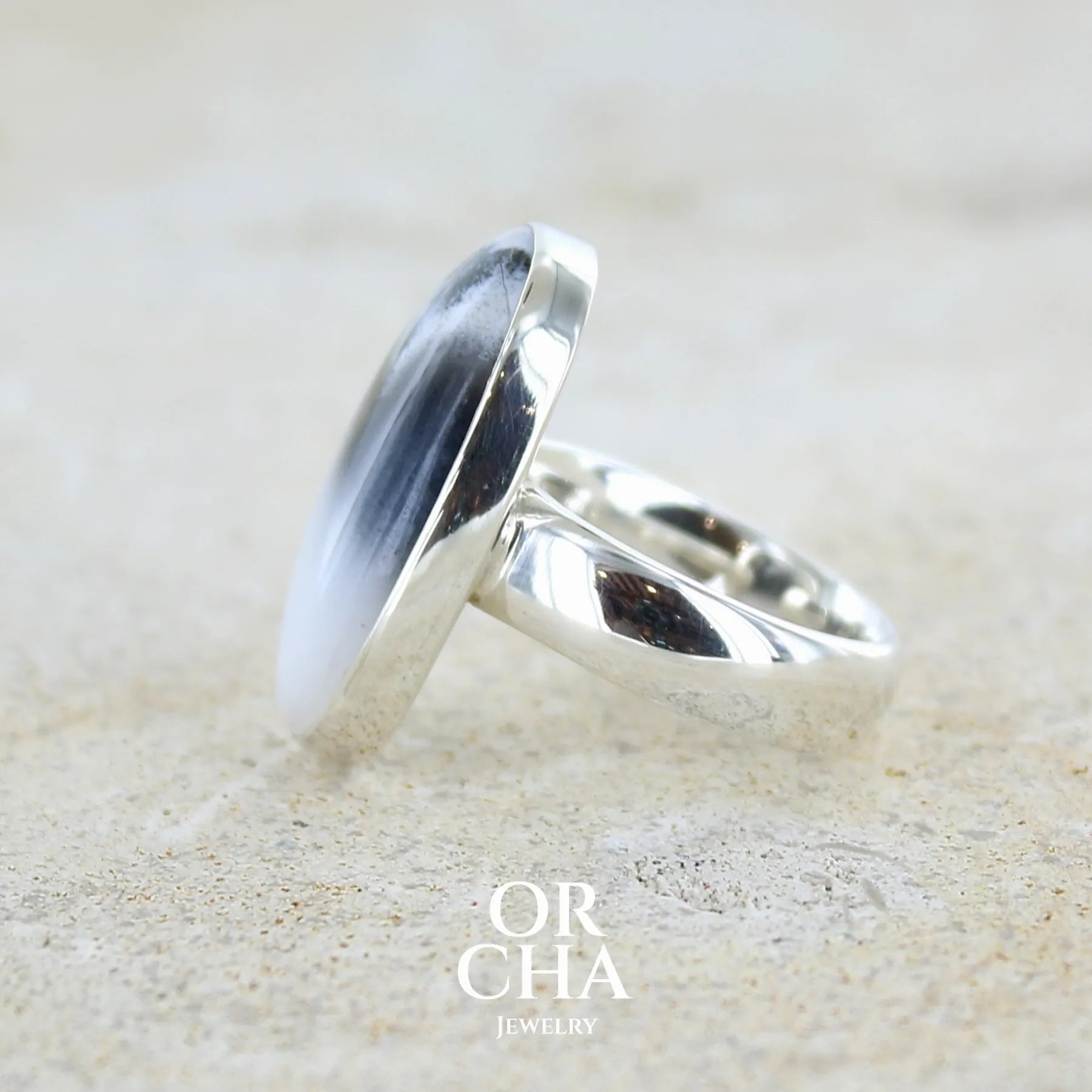 Détail du sertissage d'une bague pour femme en argent massif sertie d'un cabochon ovale d'agate dendritique de couleur blanc pur et noir. Pierre opaque translucide à inclusions paysages de dendrites de manganèse noires contrastées. Bijou unique réalisée en taille 54 par Orchajewelry