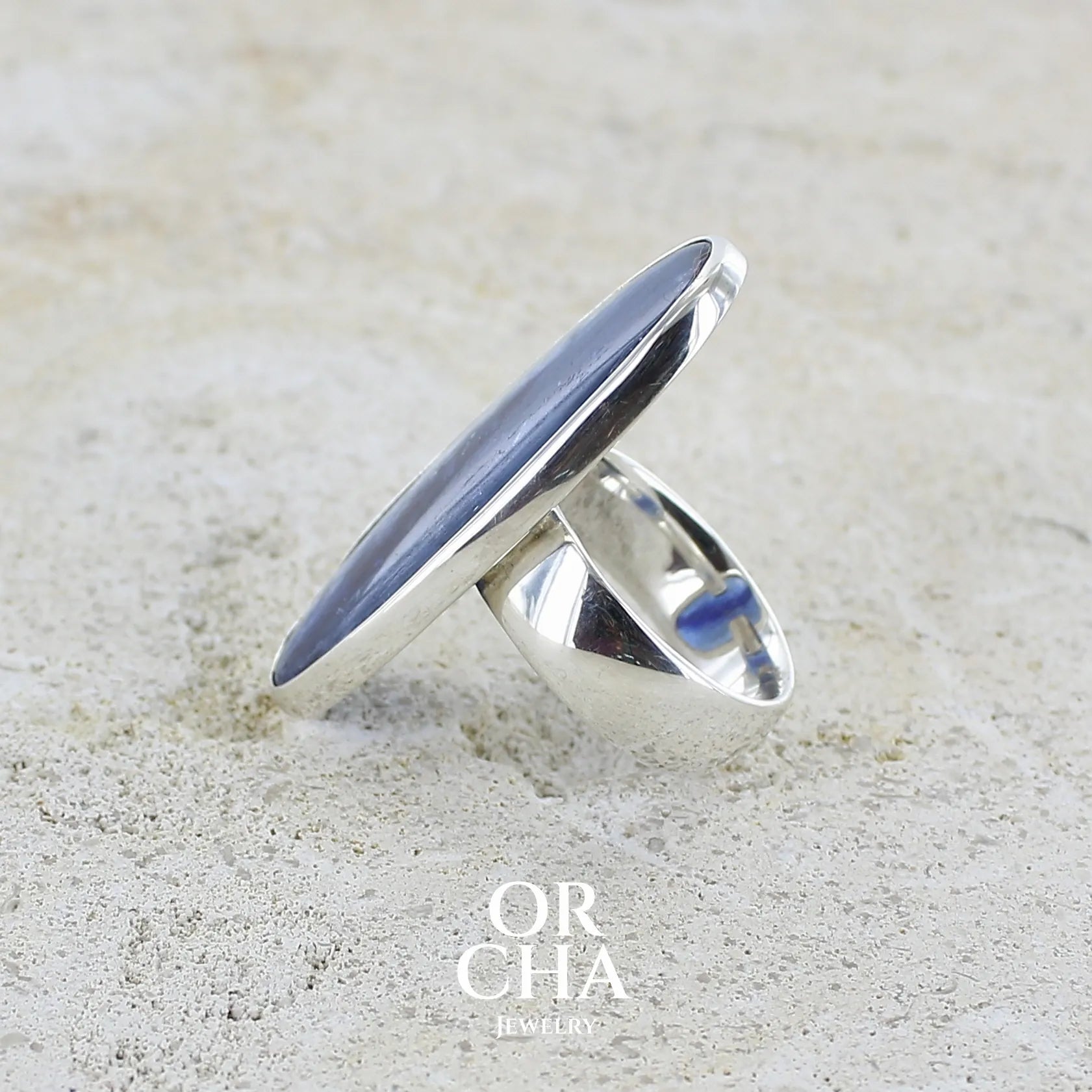 sertissage d'une grande bague pour femme en argent massif, sertie d'un long cabochon ovale de cyanite de couleur bleu denim nacré. Pierre de qualité translucide. Bijou unique réalisée en taille 58 par Orcha jewelry