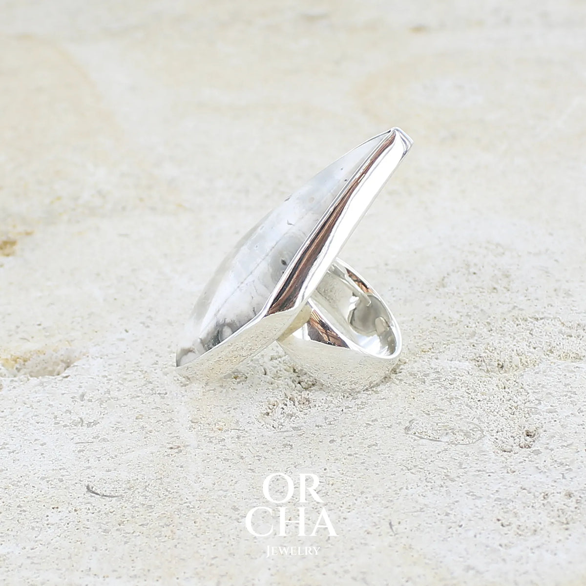 Détail du sertissage d'une grande bague pour femme en argent massif sertie d'un cabochon de jaspe orbiculaire de couleur crème, kaki et gris. Pierre naturelle de qualité opaque taillée en forme de losange, Bijou unique réalise en taille 56 par Orcha Jewelry