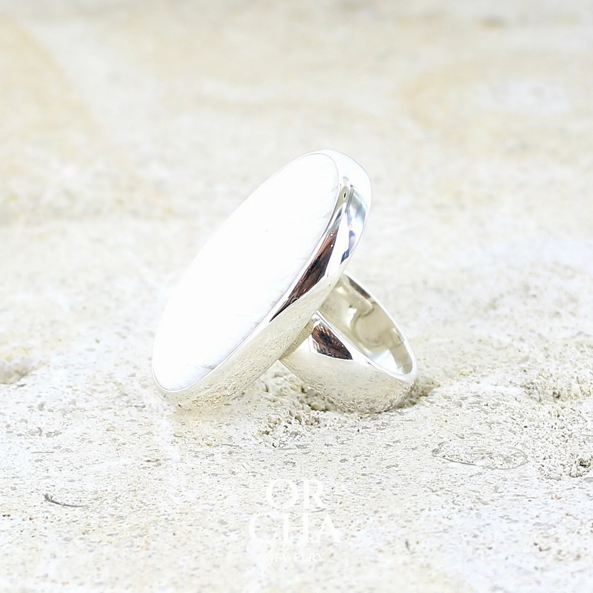 sertissage d'une bague pour femme en argent massif sertie d'un cabochon de scolecite de couleur blanc pur. Pierre naturelle de qualité opaque taillée en ovale. Bague unique réalisée en taille 58 par Orcha jewelry