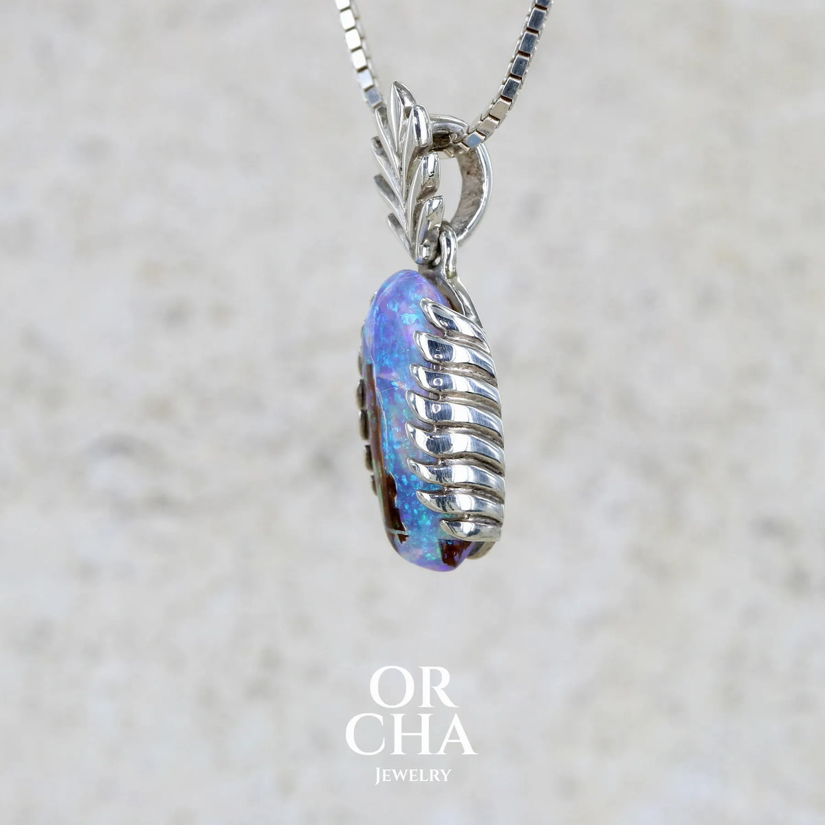 détail du sertissage d'un pendentif pour femme en argent massif 925 serti d'une opale cristal aux feux étoilés multicolores à dominante bleu violet et vert. Cabochon de 3,2 carats taillé de forme oval de qualité transparente. Bijou unique réalisé par Orchajewelry