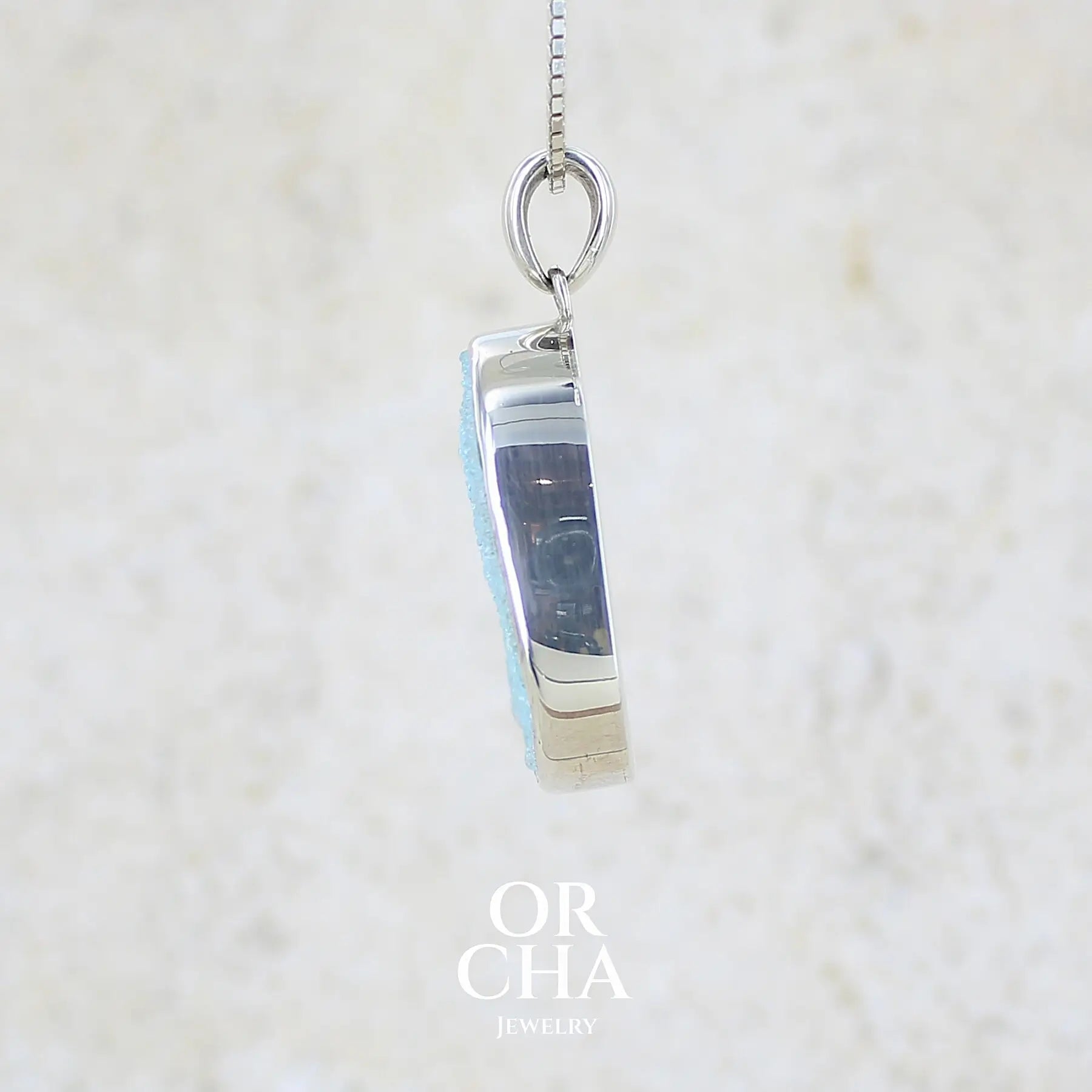 détail sertissage d'un pendentif pour femme en argent massif sertie d'un magnifique gemsilica druzy, chrysocolle silicifiée recouverte de fins cristaux de quartz scintillant. Pierre de qualité opaque taillée en tranche de forme ovale. Pierre naturelle originaire de République dominicaine du Congo de couleur bleu clair turquoise. pierre rare et unique
