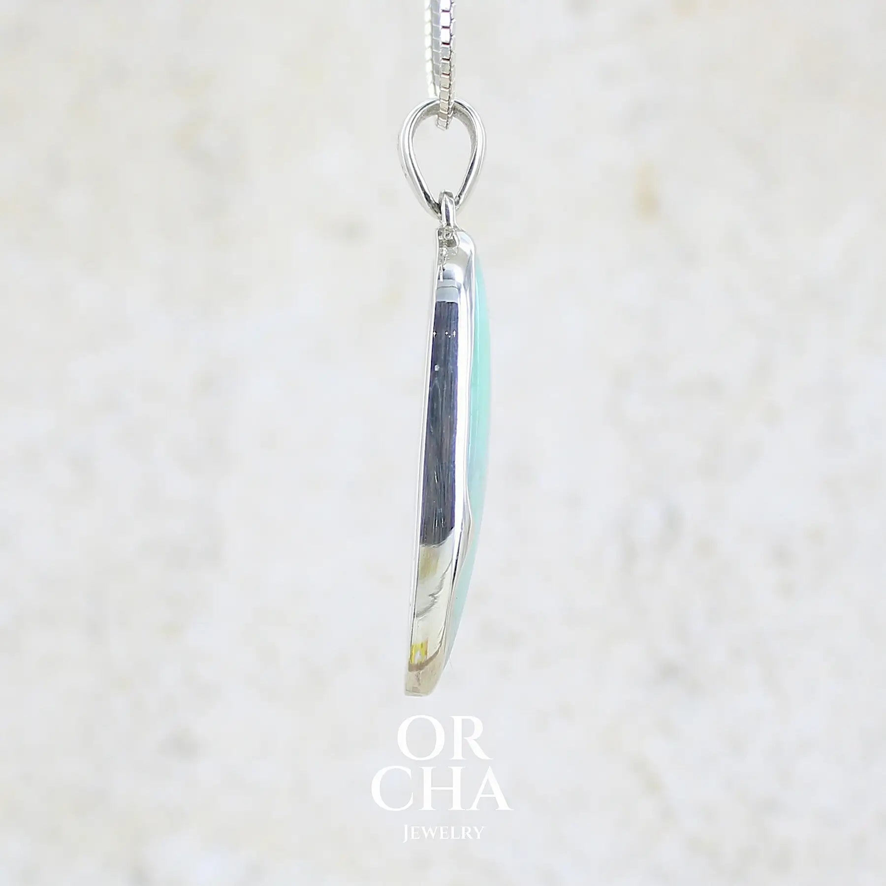 détail du sertissage d'un pendentif pour femme et homme en argent massif, sertie d'un cabochon d'opale bleue du Pérou de couleur verte bleutée. Pierre en forme de goutte inversée. Pierre opaque et translucide. Bijoux unique, éthique et durable présenté dans un coffret de notre marque, prêt à offrir. Livraison offerte, certificat d'authenticité, service client.