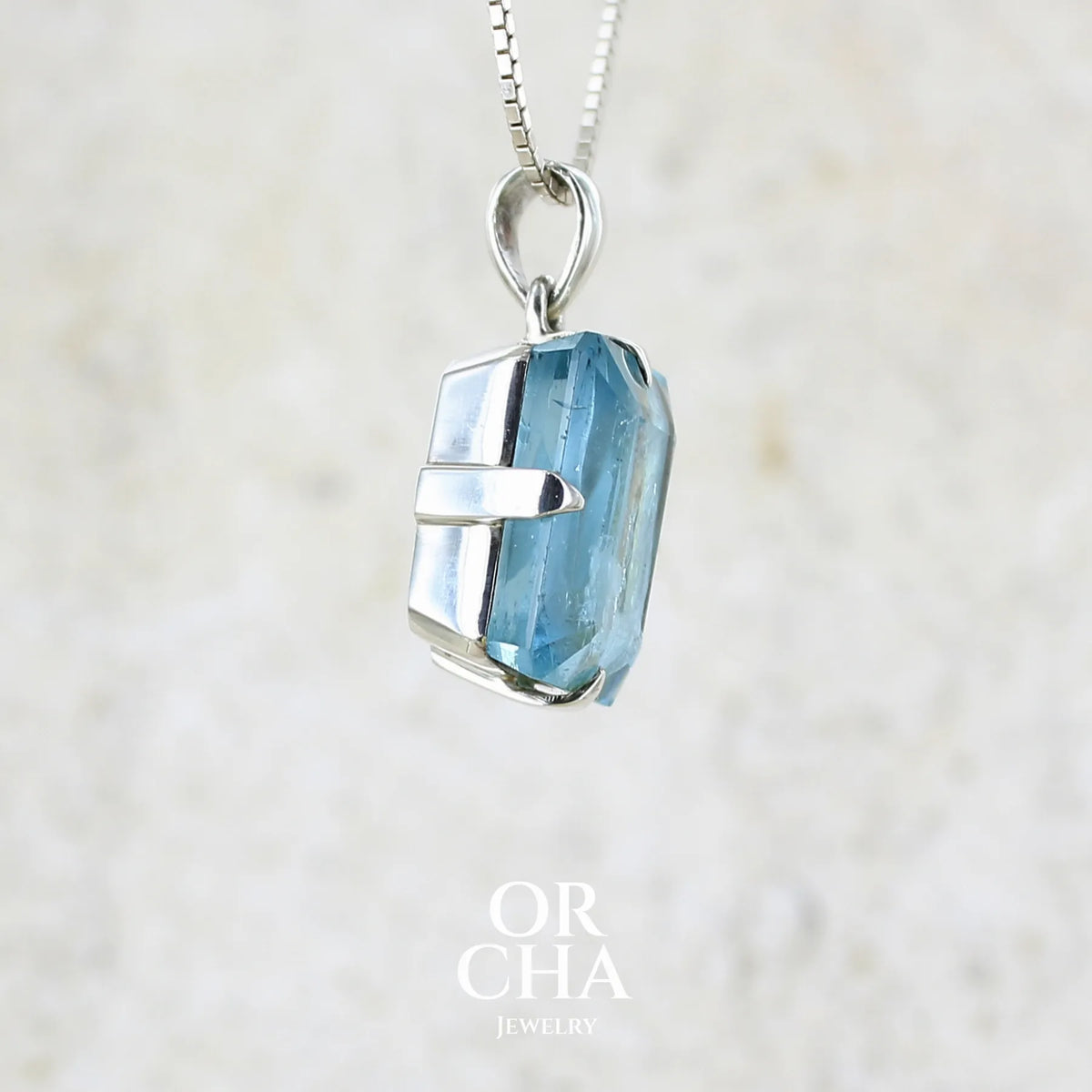 detail du sertissage d'un pendentif unisexe en argent massif sertie d'une aigue marine taillée de 17 carats de couleur bleu foncé profond et intense, pierre transparente avec de grosses inclusions. Pierre naturelle facettée de forme rectangulaire. Bijoux unique réalisée par Orchajewelry