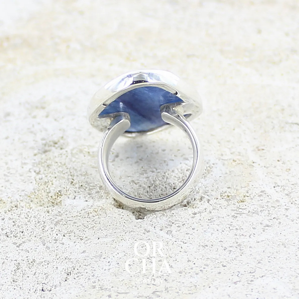 Vue de dos d'une bague pour femme en argent massif sertie d'un cabochon de cyanite de couleur bleu jean nacré. Pierre translucide à inclusions. Bijou unique réalisée en taille 54 par Orcha Jewelry