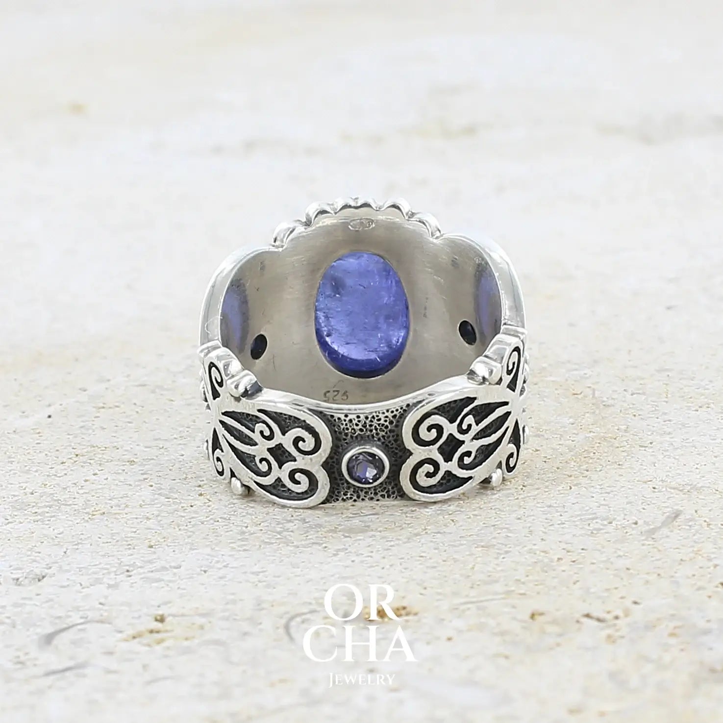 vue de dos d'une bague en argent massif sculptées d'entrelacs de style celtique qui illustrent des papillons, sertie d'une Tanzanite. Pierre cabochon de forme ovale, de couleur bleu lavande foncé, de qualité transparente avec inclusions. Taille 56. Bijoux unique, éthique et durable présenté dans un coffret de notre marque, prêt à offrir. Livraison offerte, certificat d'authenticité, service client.