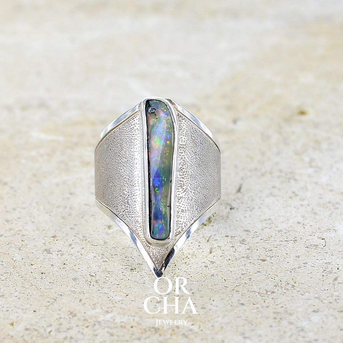 Bague plastron pour femme en argent massif 925 sertie d'une opale boulder aux feux multicolores. Cabochon d'opale massive naturelle, de qualité opaque. Bijoux unique réalisé en taille 59 par Orcha Jewelry.