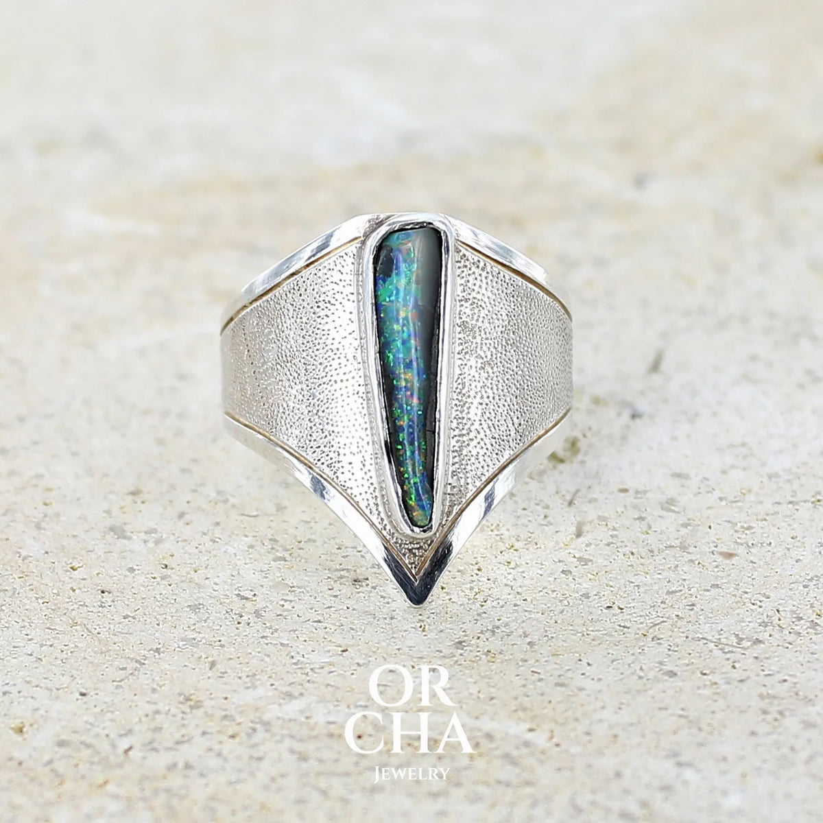 Bague pour femme en argent massif 925 sertie d'une opale boulder aux feux multicolores. Cabochon d'opale massive naturelle taillée en forme d'aile. Pierre de qualité opaque. Bijoux unique réalisé en taille 58 par Orcha Jewelry.