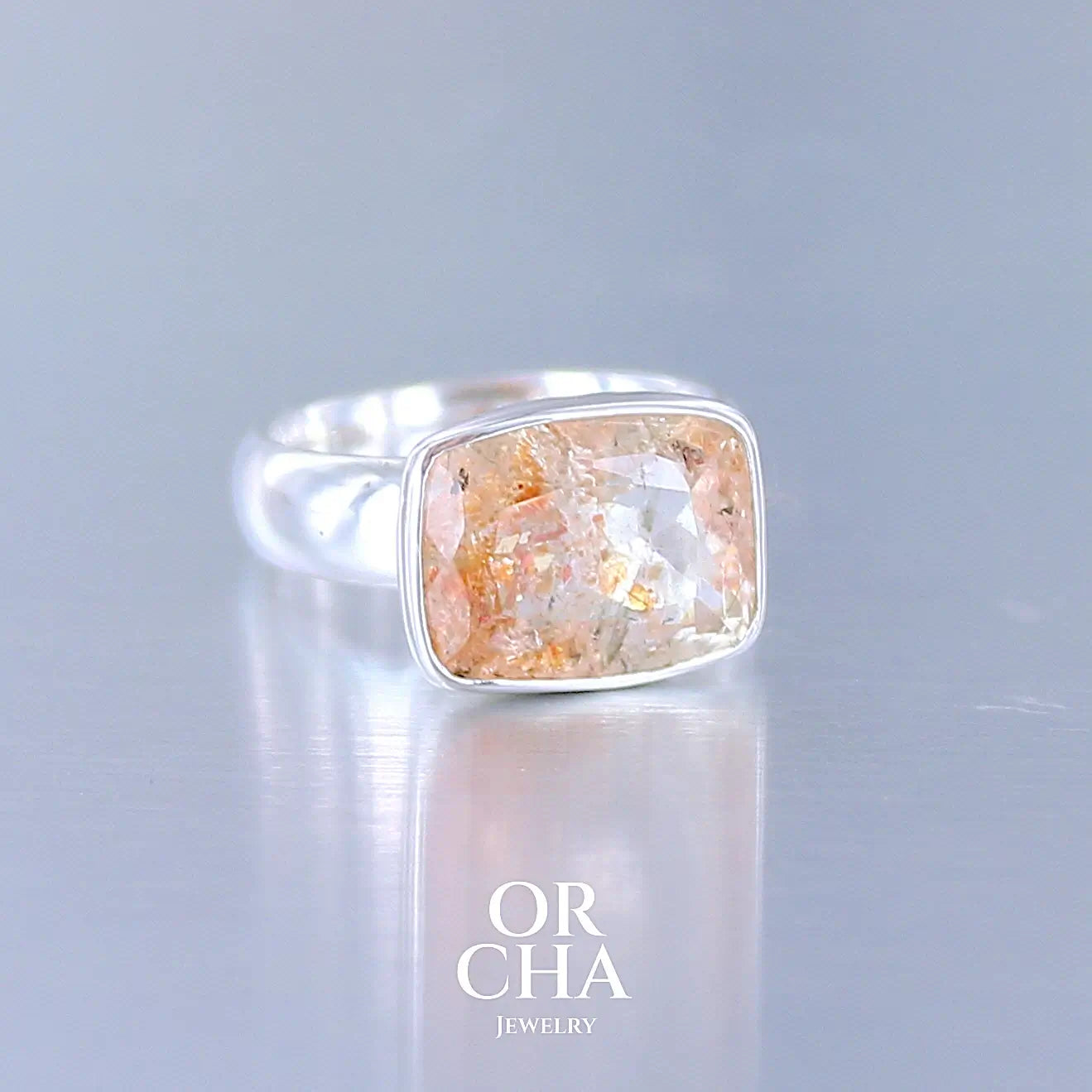 Profil d'une bague cocktail pour femme en argent massif sertie d'une pierre de soleil oranges de très belle qualité, pierre transparente avec inclusions scintillantes d'hématites.Pierre naturelle facettée de forme rectangulaire. Tailles 54. Bijoux unique, éthique et durable présenté dans un coffret de notre marque, prêt à offrir. Livraison offerte, certificat d'authenticité, service client.