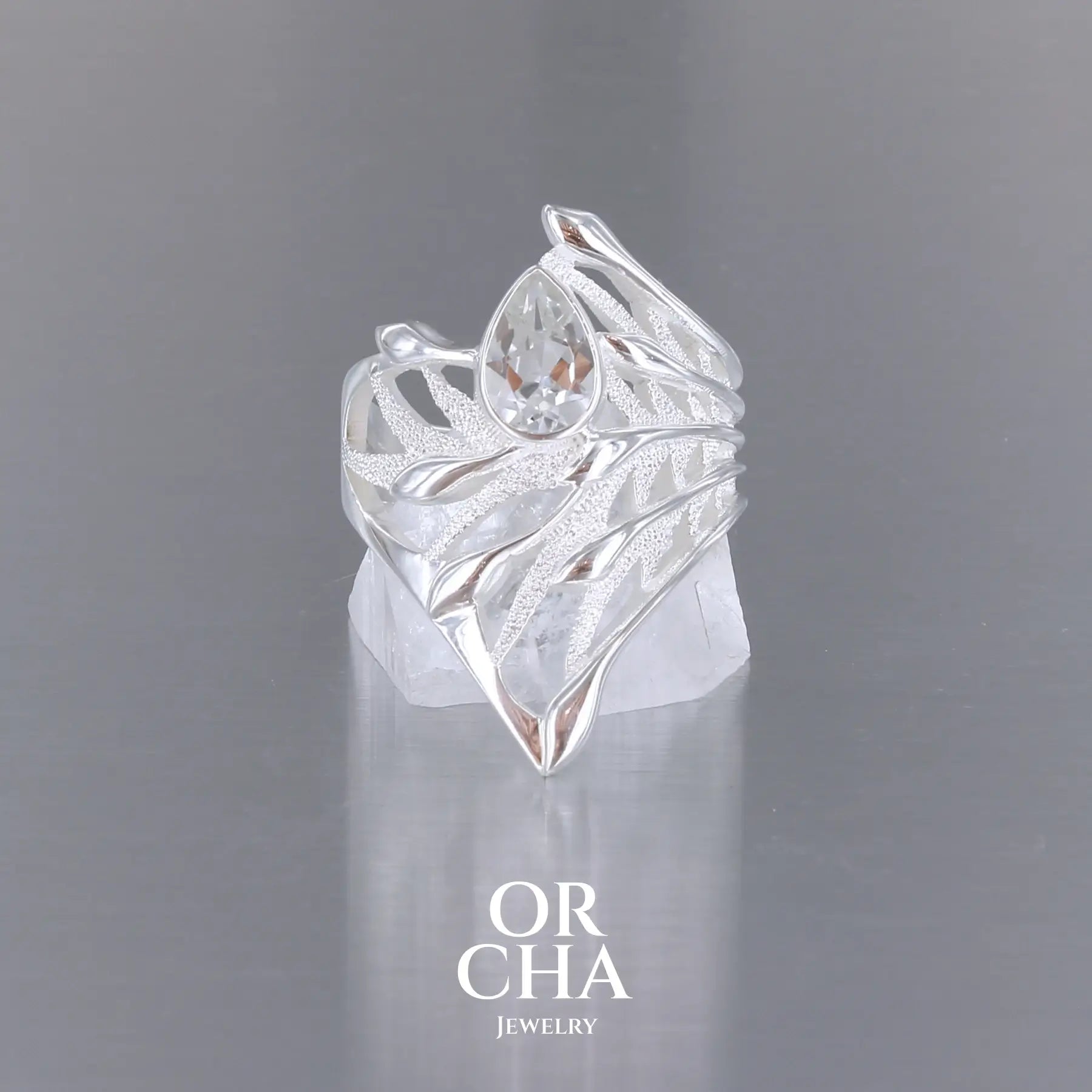 Grande Bague Jungle illustrant un feuillage tropicale, pour femme, en argent massif sertie d'une Topaze blanche facettée en forme de goutte. Pierre incolore, très lumineuse et propre à l'oeil. Disponible en plusieurs tailles. Bijoux unique, éthique et durable présenté dans un coffret de notre marque, prêt à offrir. Livraison offerte, certificat d'authenticité, service client.
