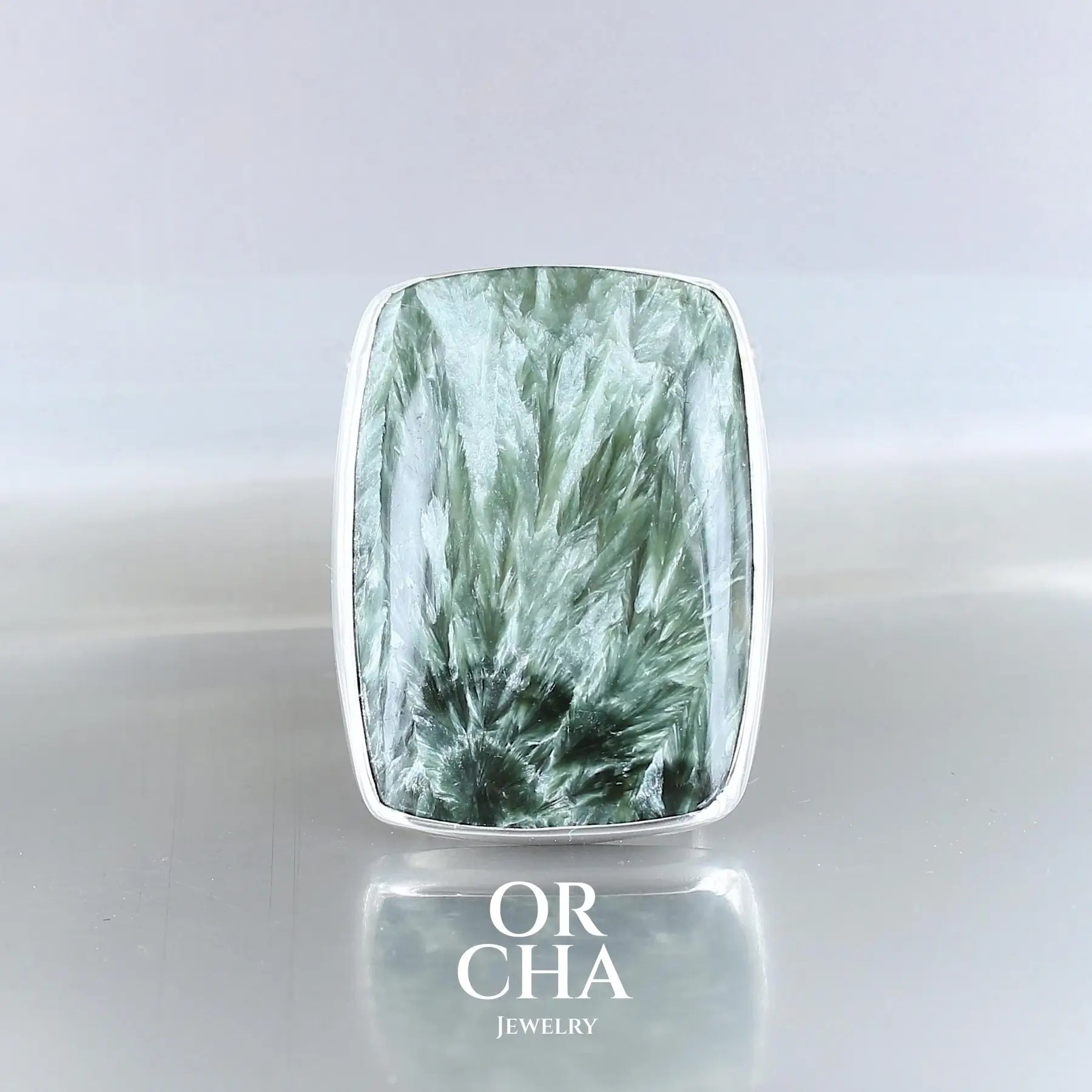 Grande bague pour femme en argent massif sertie d'une séraphinite de couleur vert kaki avec chatoyance argenté. Cabochon rectangulaire, pierre naturelle de qualité opaque.Taille 56. Bijoux unique, éthique et durable présenté dans un coffret de notre marque, prêt à offrir. Livraison offerte, certificat d'authenticité, service client.