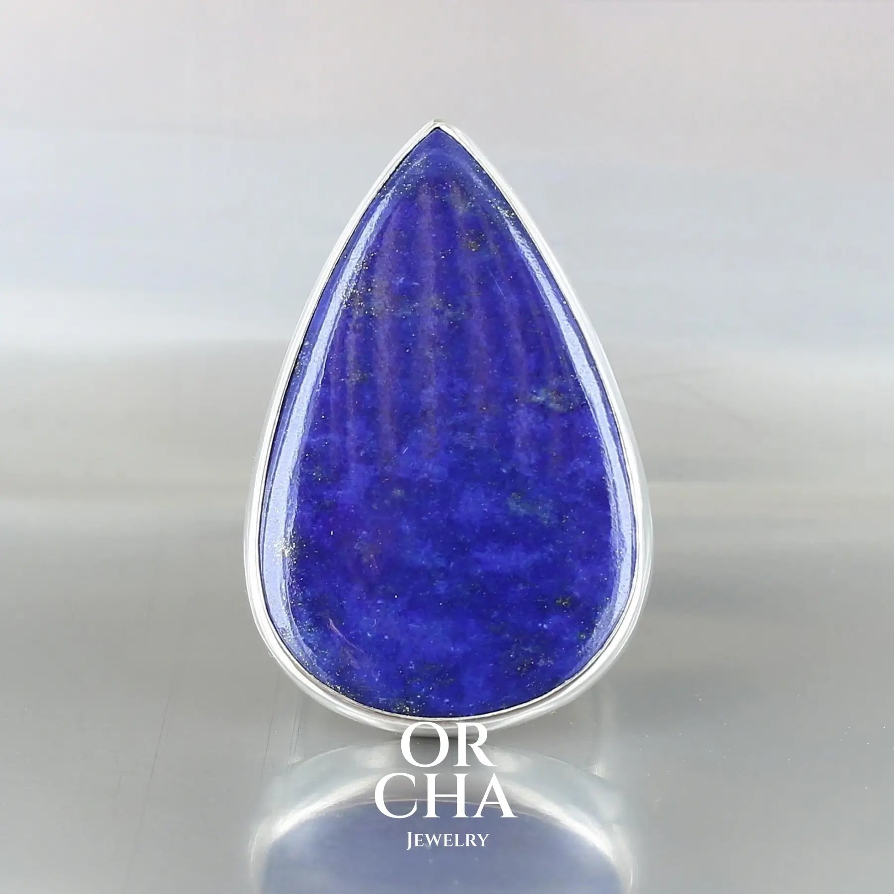 Grande bague pour femme en argent massif sertie d'un Lapis Lazuli de couleur bleu nuit moucheté d'éclats de pyrite dorée. Pierre naturelle taillée cabochon en forme de goutte de qualité opaque. Taille 58. Bijoux unique, éthique et durable présenté dans un coffret de notre marque, prêt à offrir. Livraison offerte, certificat d'authenticité, service client