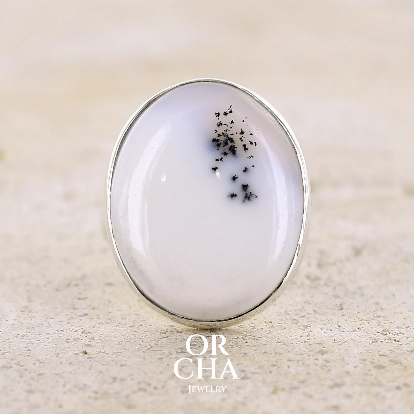 Bague pour femme en argent massif sertie d'un cabochon ovale d'agate dendritique de couleur blanc pur. Pierre opaque translucide à inclusions de dendrites de manganèse noires contrastées. Bijou unique réalisée en taille 56,5 par Orchajewelry