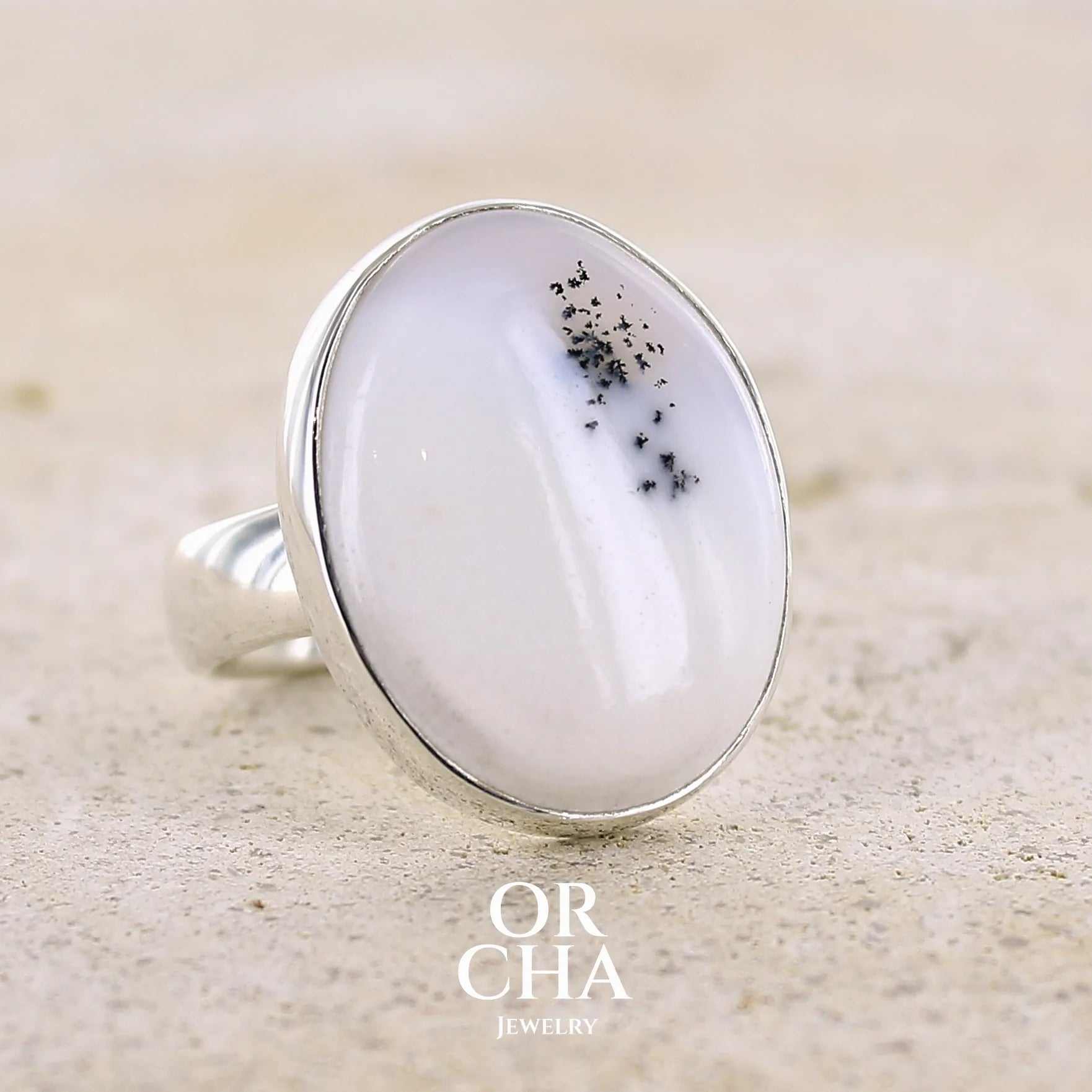 Bague pour femme en argent massif sertie d'un cabochon ovale d'agate dendritique de couleur blanc pur. Pierre opaque translucide à inclusions de dendrites de manganèse noires contrastées. Bijou unique réalisée en taille 56,5 par Orchajewelry