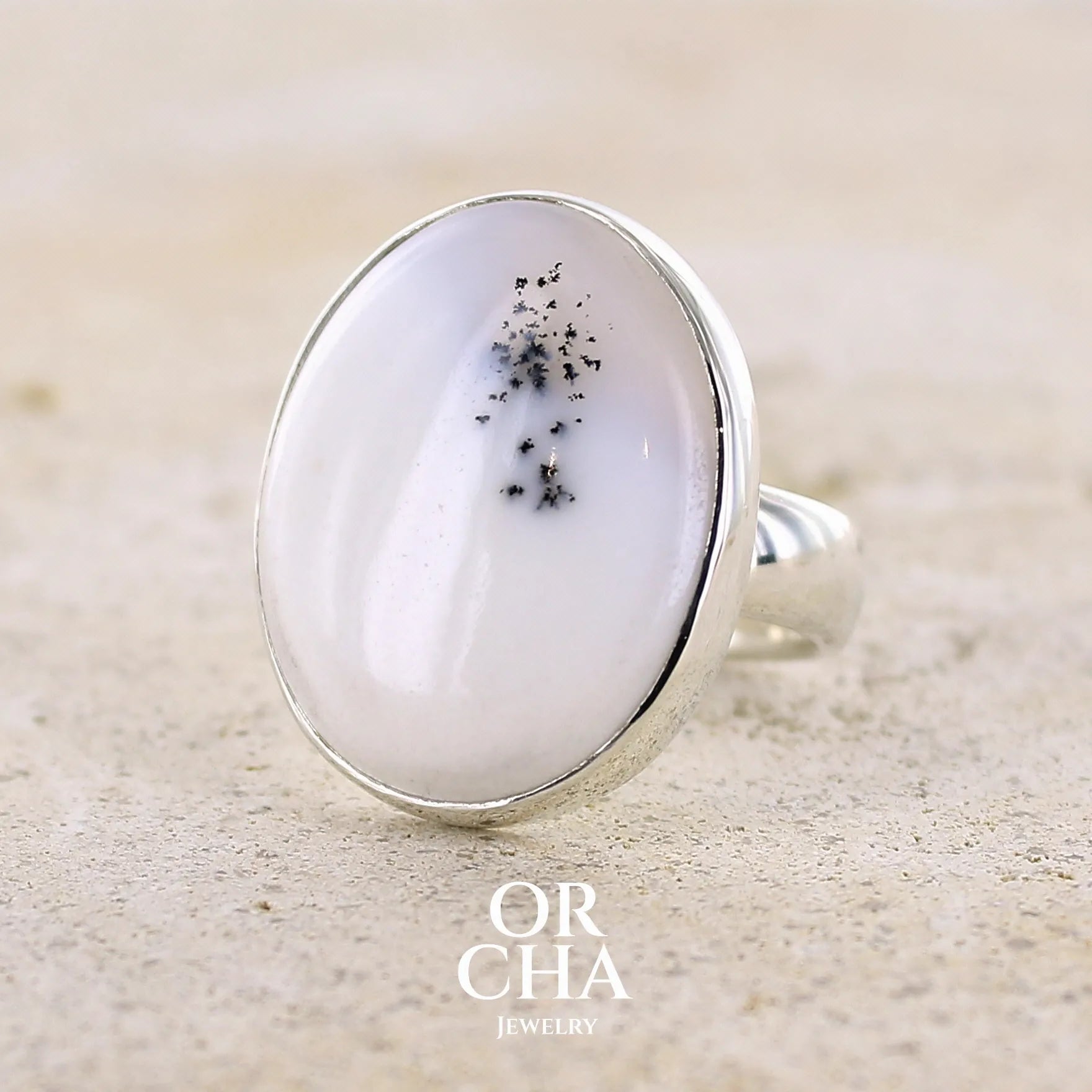Bague pour femme en argent massif sertie d'un cabochon ovale d'agate dendritique de couleur blanc pur. Pierre opaque translucide à inclusions de dendrites de manganèse noires contrastées. Bijou unique réalisée en taille 56,5 par Orchajewelry