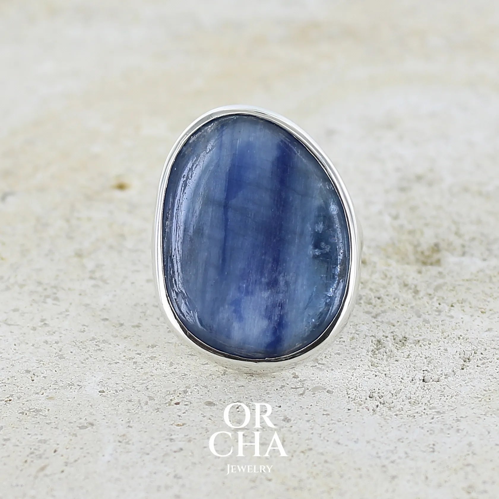 Bague pour femme en argent massif sertie d'un cabochon de cyanite de couleur bleu jean nacré. Pierre translucide à inclusions. Bijou unique réalisée en taille 55 par Orcha Jewelry