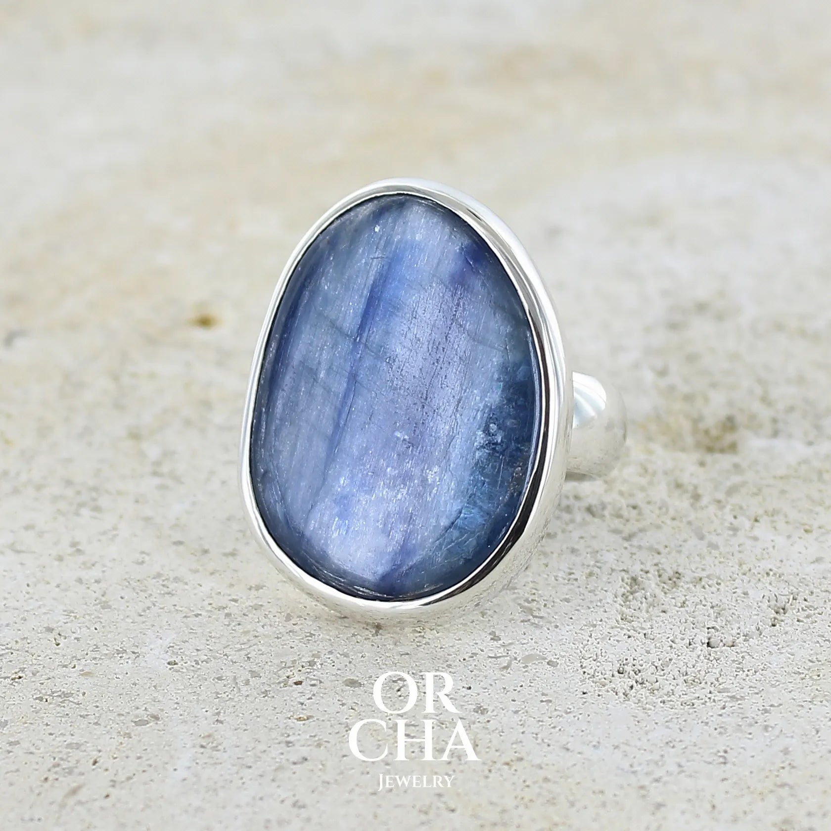 Bague pour femme en argent massif sertie d'un cabochon de cyanite de couleur bleu jean nacré. Pierre translucide à inclusions. Bijou unique réalisée en taille 55 par Orcha Jewelry