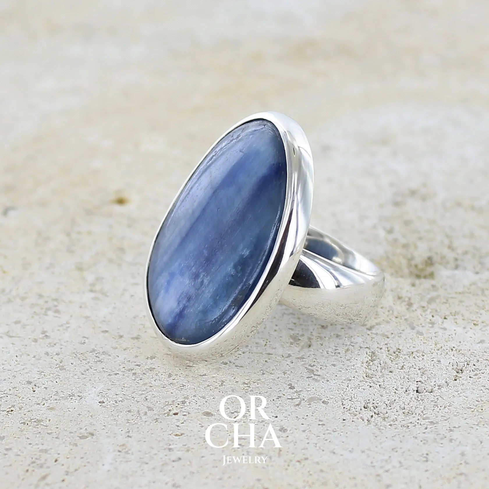 Bague pour femme en argent massif sertie d'un cabochon de cyanite de couleur bleu jean nacré. Pierre translucide à inclusions. Bijou unique réalisée en taille 55 par Orcha Jewelry