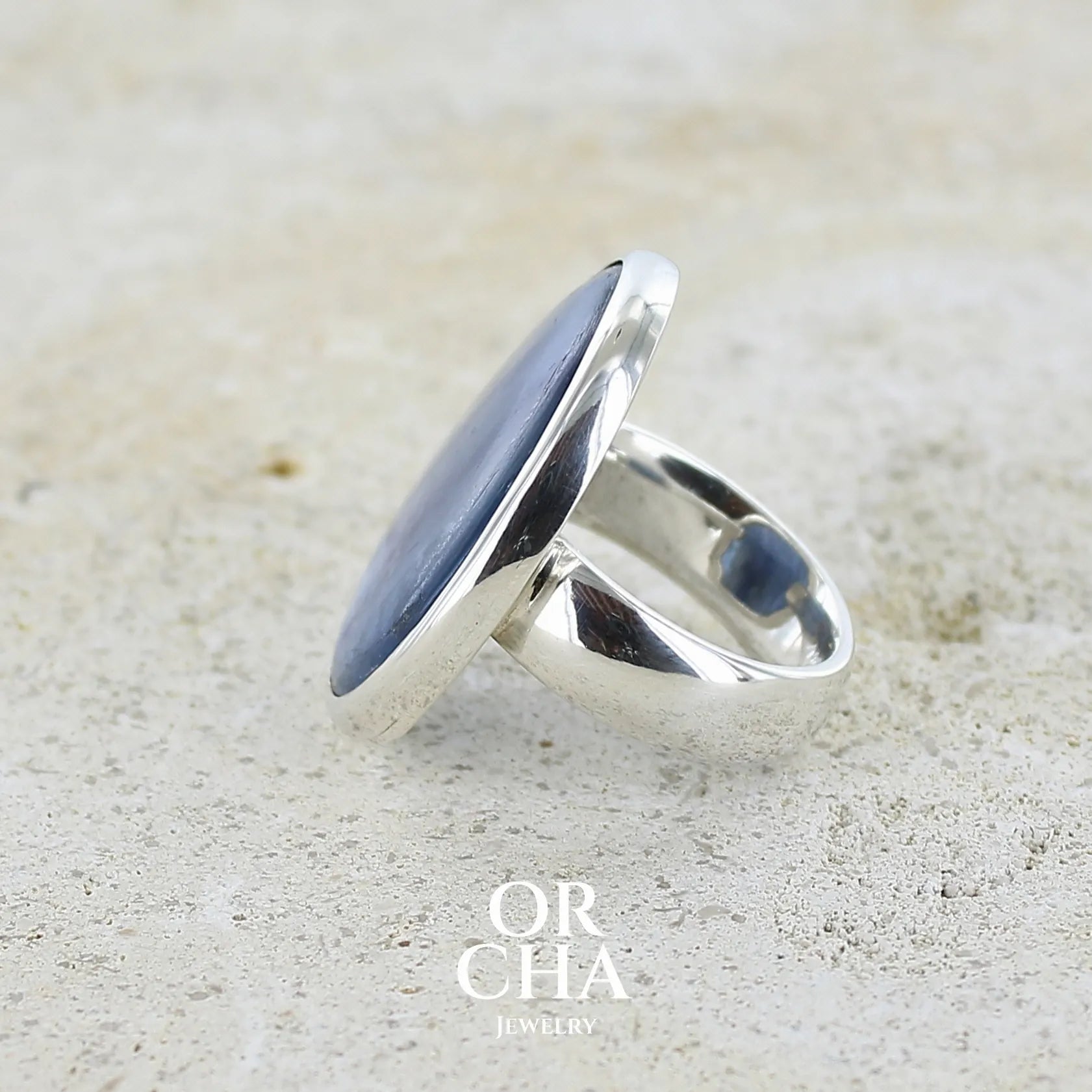 Bague pour femme en argent massif sertie d'un cabochon de cyanite de couleur bleu jean nacré. Pierre translucide à inclusions. Bijou unique réalisée en taille 55 par Orcha Jewelry