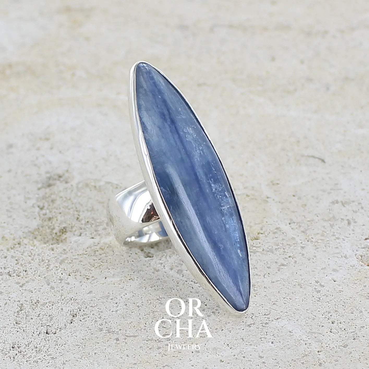 Bague marquise pour femme en argent massif sertie d'un cabochon de cyanite de couleur bleu jean nacré. Pierre translucide à inclusions. Bijou unique réalisée en taille 58 par Orchajewelry
