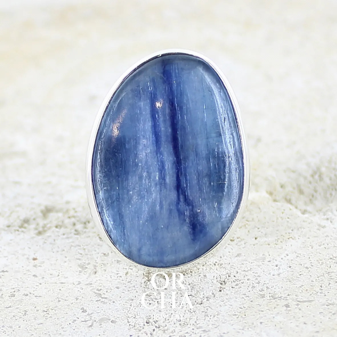 Bague pour femme en argent massif sertie d'un cabochon de cyanite de couleur bleu jean irisée. Pierre translucide à inclusions. Bijou unique réalisée en taille 56 par Orcha Jewelry