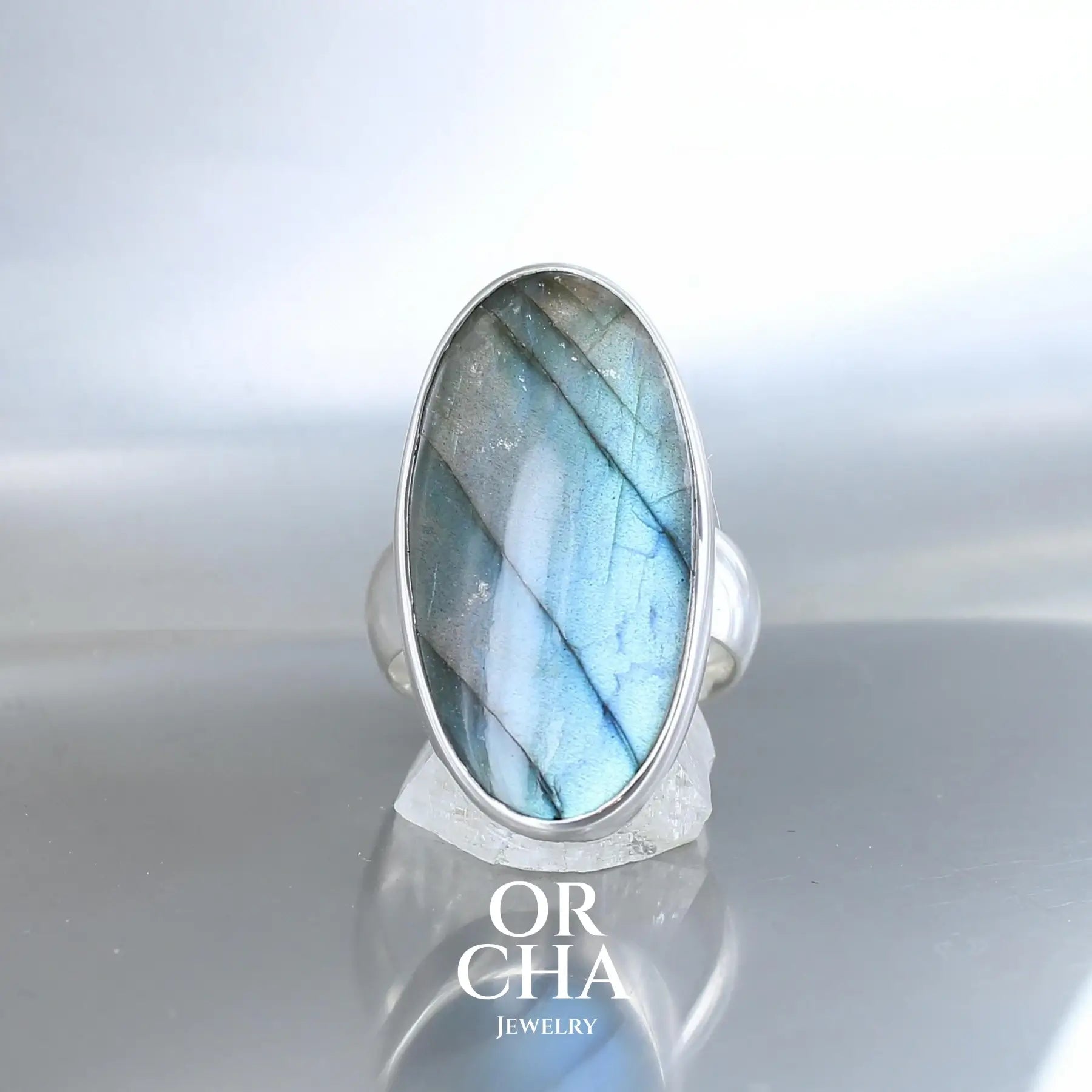 Bague pour femme en argent massif serti d'une labradorite bleue aux reflets bleus à verts selon l'angle de vision,  Pierre cabochon naturelle translucide présentant des inclusions fréquents sur ce type de pierre. Taille 61. Bijoux unique, éthique et durable présenté dans un coffret de notre marque, prêt à offrir. Livraison offerte, certificat d'authenticité, service client.