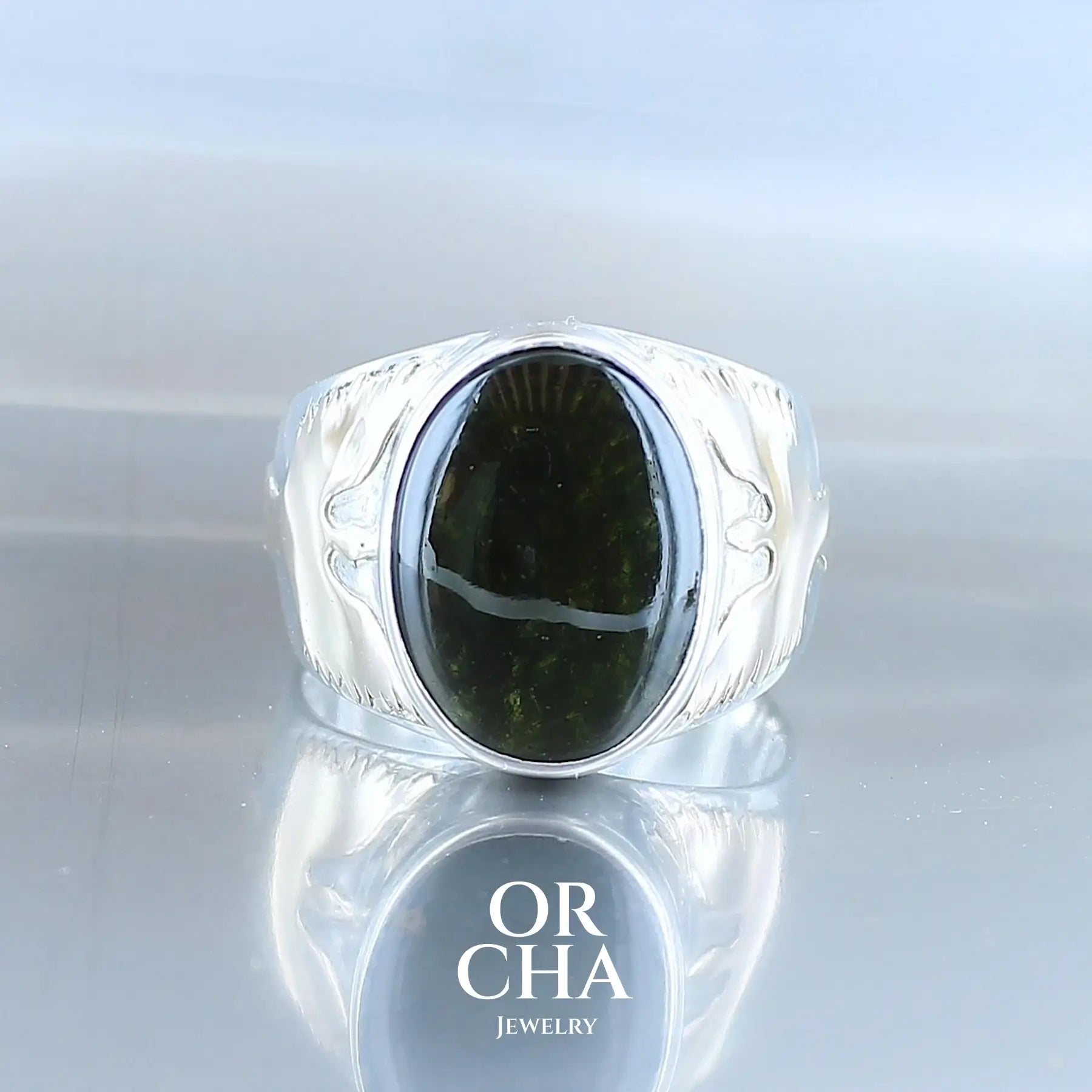 Bague pour homme en argent massif et or 9k où s'illustrent de chaque cotés de la bague des Phoenix en or. Cette bague est sertie d'un cabochon de moldavite de couleur vert foncé. Pierre  naturelle transparente qui laisse voir le fond de la pierre laissé brute. Taille 67. Bijoux unique, éthique et durable présenté dans un coffret de notre marque, prêt à offrir. Livraison offerte, certificat d'authenticité, service client.