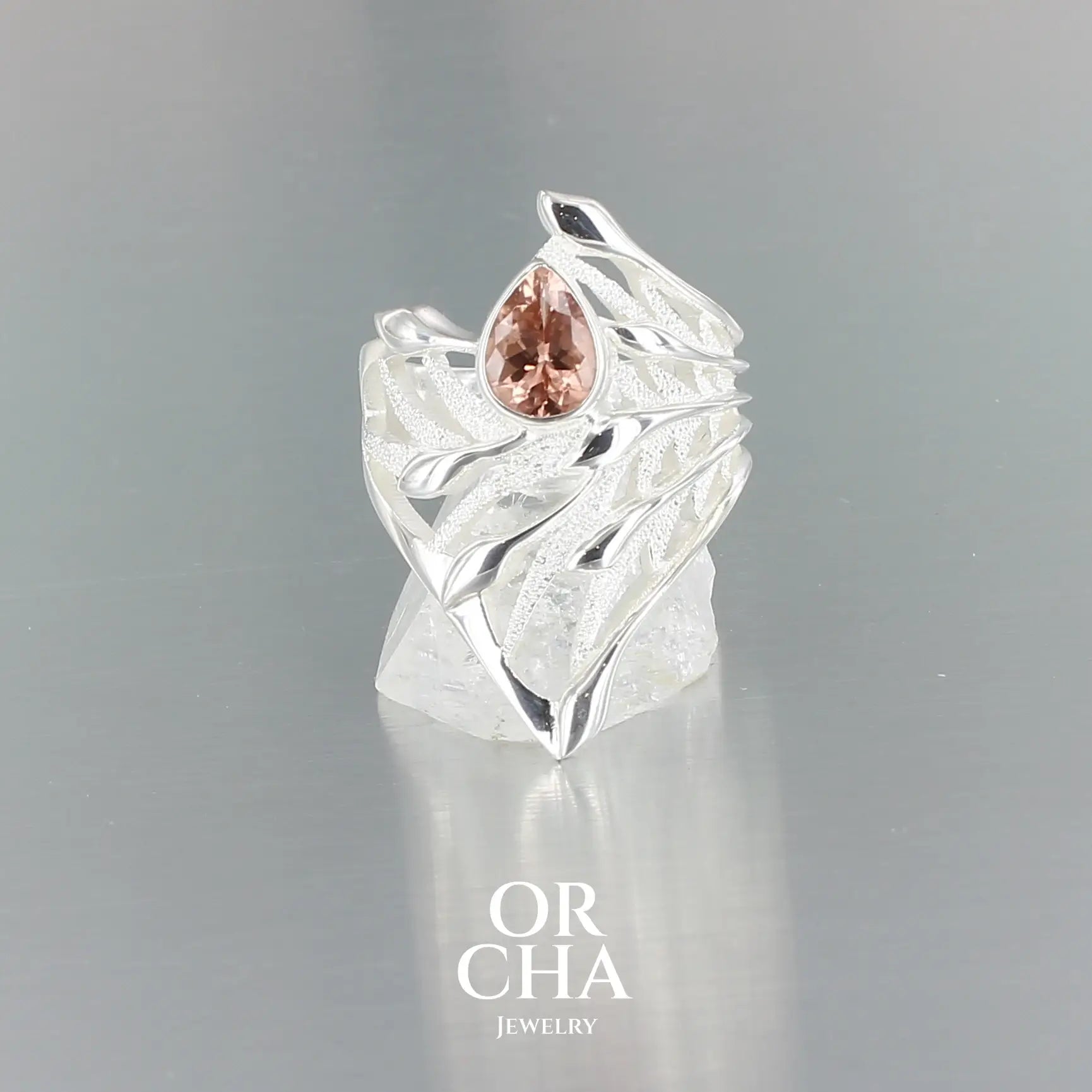 Bague en argent massif présentant un design sculptural évoquant un entrelacs une feuille stylisée, alternant entre surfaces lisses polies et zones texturées satinées. En son centre est sertie une tourmaline rose taille poire, lumineuse, aux reflets délicats. Bague réalisée en taille 54. Bijoux unique, éthique et durable présenté dans un coffret de notre marque, prêt à offrir. Livraison offerte, certificat d'authenticité, service client.