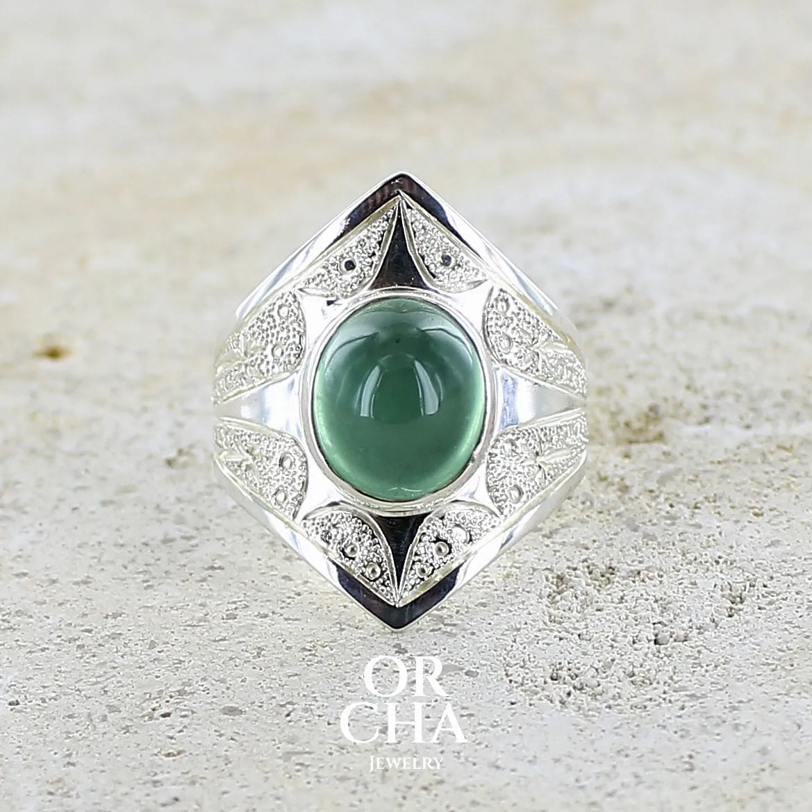 Bague pour femme en argent massif sculptées d'étoiles et autres corps célestes sertie d'un cabochon ovale de préhnite de couleur verte pastel lumineuse. Pierre naturelle de qualité transparente présentant des inclusions. Bijoux unique réalisé en taille 57 par Orchajewelry.