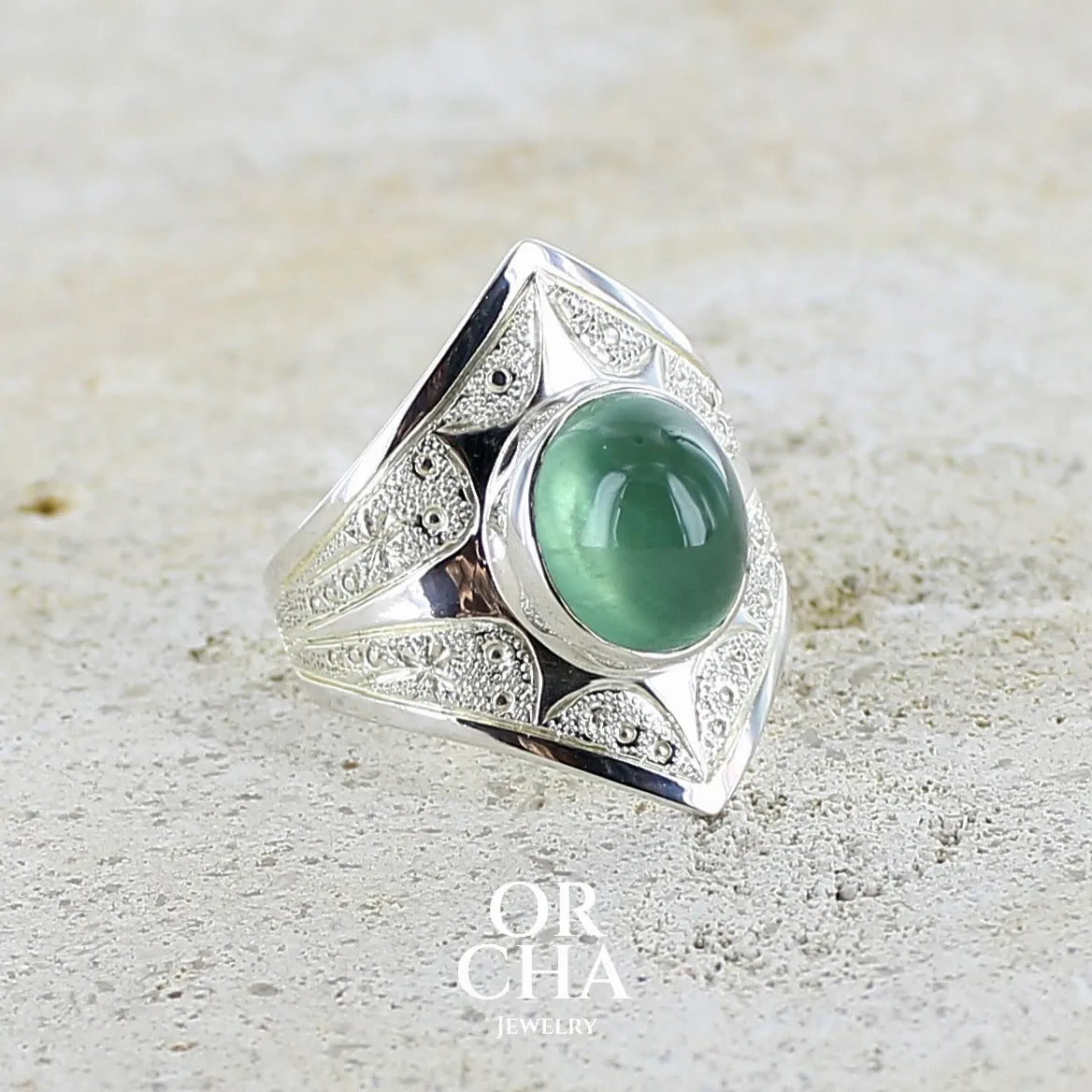 Bague pour femme en argent massif sculptées d'étoiles et autres corps célestes sertie d'un cabochon ovale de préhnite de couleur verte pastel lumineuse. Pierre naturelle de qualité transparente présentant des inclusions. Bijoux unique réalisé en taille 57 par Orchajewelry.