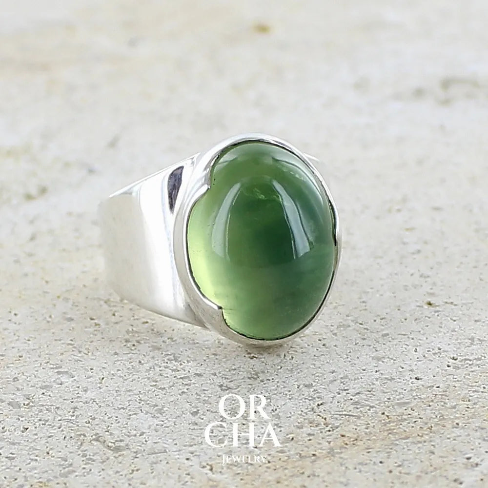 Bague pour femme en argent massif sertie d'une préhnite de couleur verte jaune clair. Pierre ovale taillée en cabochon. Pierre gemme de qualité transparente à inclusions. Bijoux unique réalisé en taille 52 par Orchajewelry.