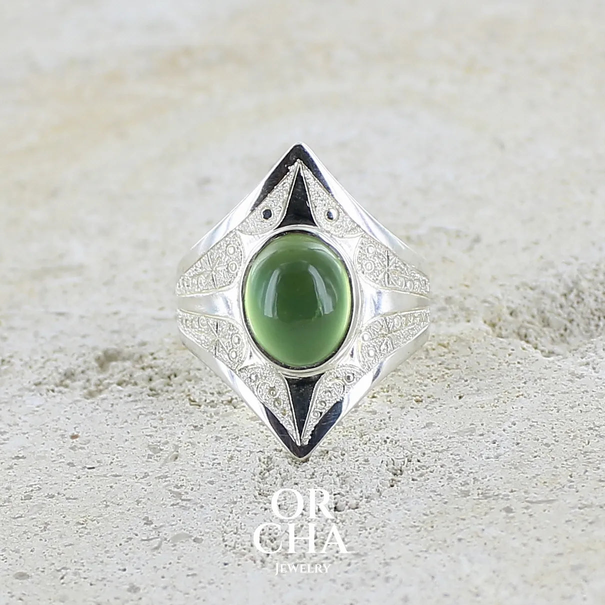 Bague pour femme en argent massif sculptées d'étoiles et autres corps célestes sertie d'un cabochon ovale de préhnite de couleur verte pastel lumineuse. Pierre naturelle de qualité transparente présentant des inclusions. Bijoux unique réalisé en taille 54,5 par Orchajewelry.