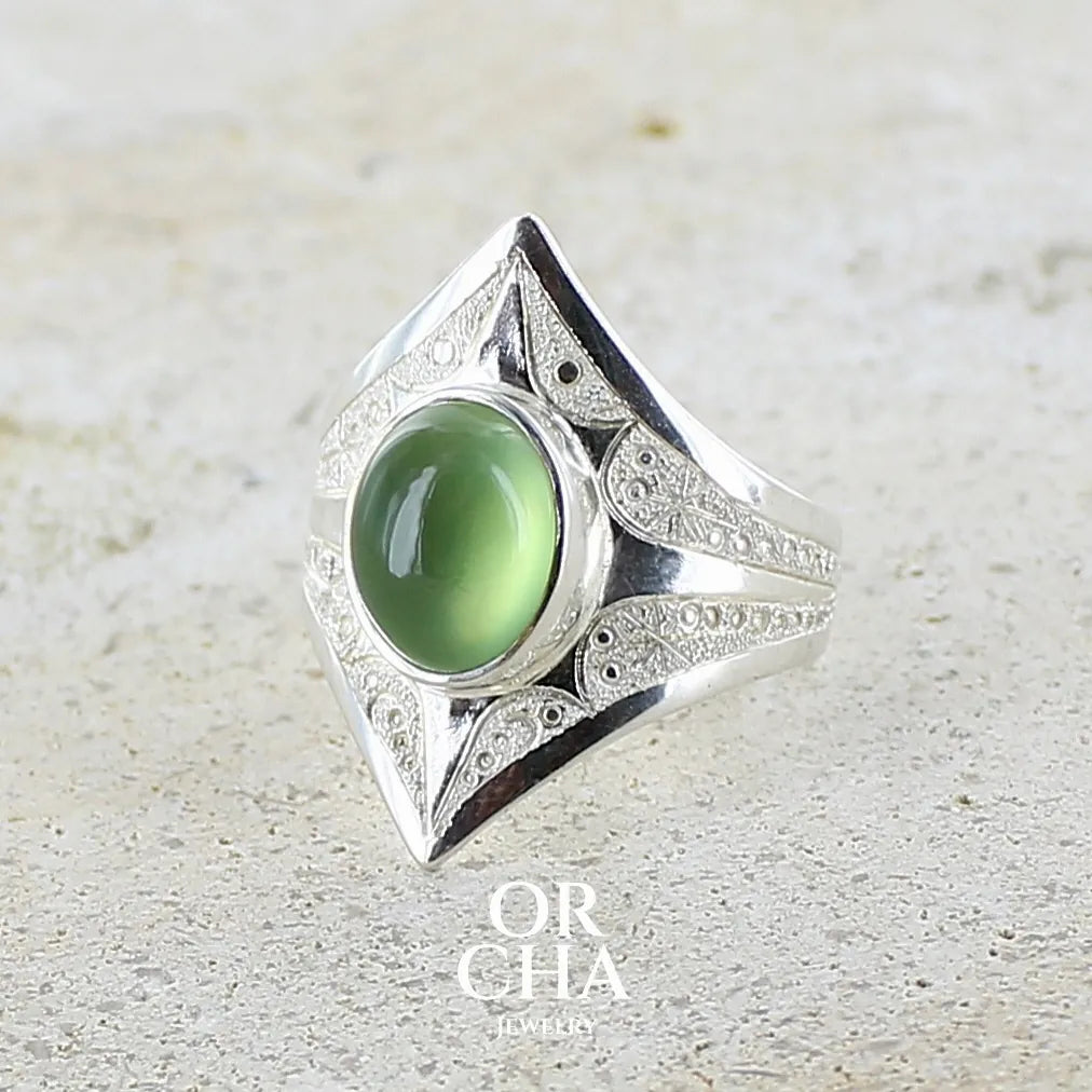 Bague pour femme en argent massif sculptées d'étoiles et autres corps célestes sertie d'un cabochon ovale de préhnite de couleur verte pastel lumineuse. Pierre naturelle de qualité transparente présentant des inclusions. Bijoux unique réalisé en taille 54,5 par Orchajewelry.