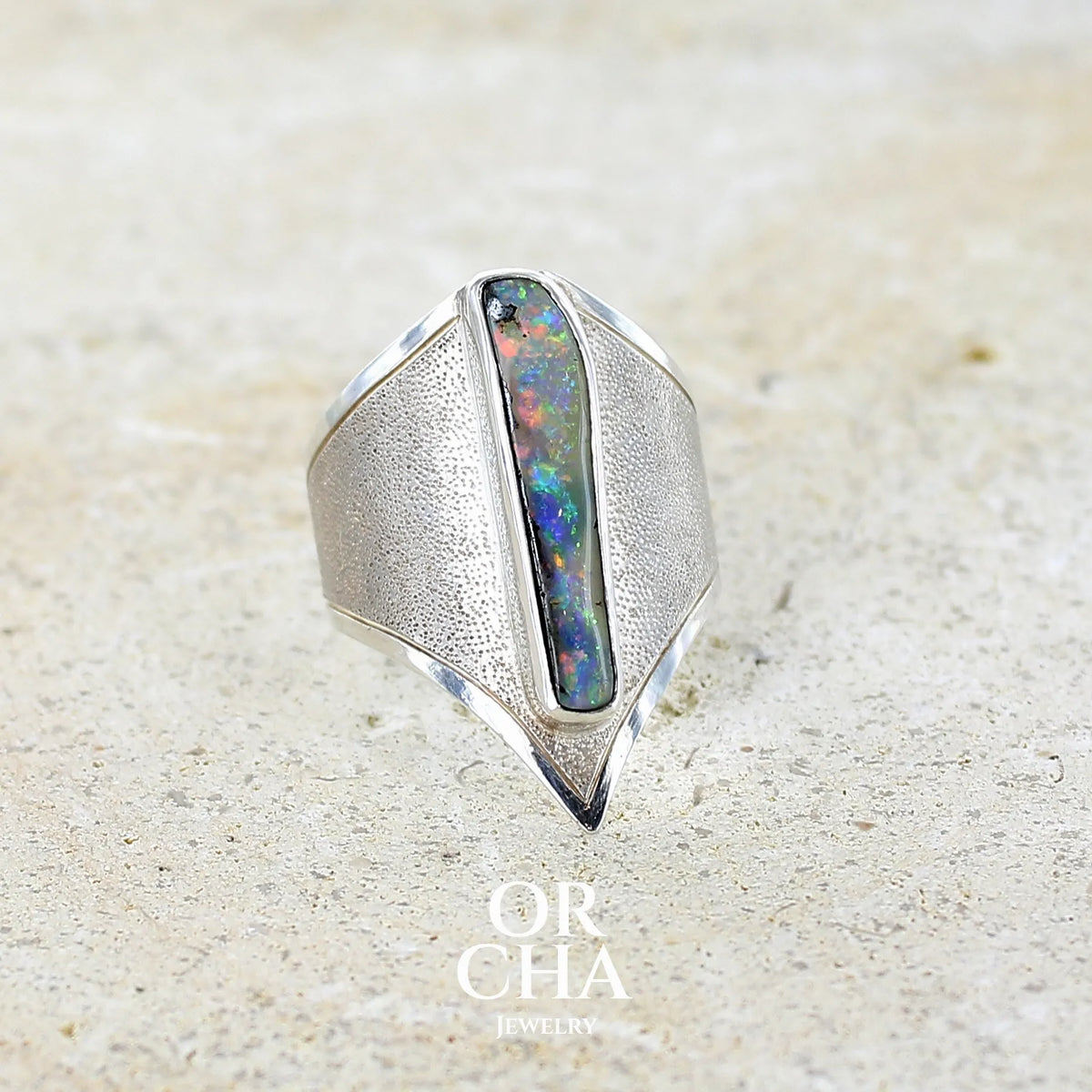 Profil droit d'une bague plastron pour femme en argent massif 925 sertie d'une opale boulder aux feux multicolores. Cabochon d'opale massive naturelle, de qualité opaque. Bijoux unique réalisé en taille 59 par Orcha Jewelry.