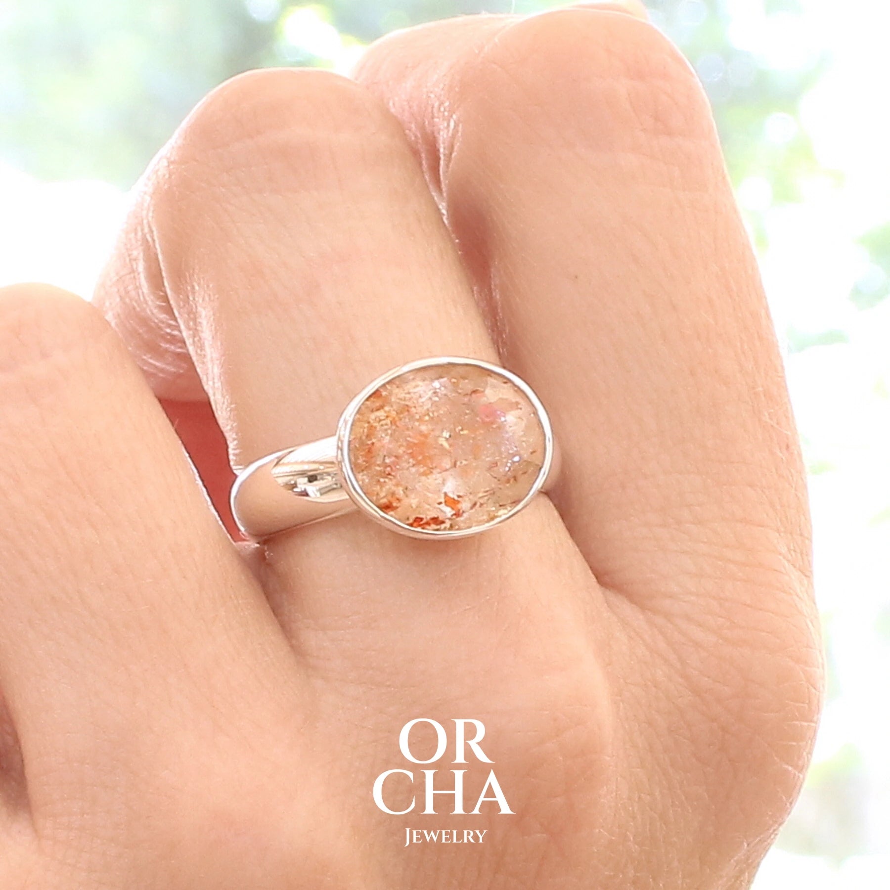 Bague cocktail pour femme en argent massif sertie d'une Pierre de soleil. Pierre ovale facettée de de couleur orange clair avec des inclusions scintillantes d'hématites. Pierre naturelle. Bijoux unique, réalisé en taille 60, éthique et durable présenté dans un coffret de notre marque, prêt à offrir. Livraison offerte, certificat d'authenticité, service client.