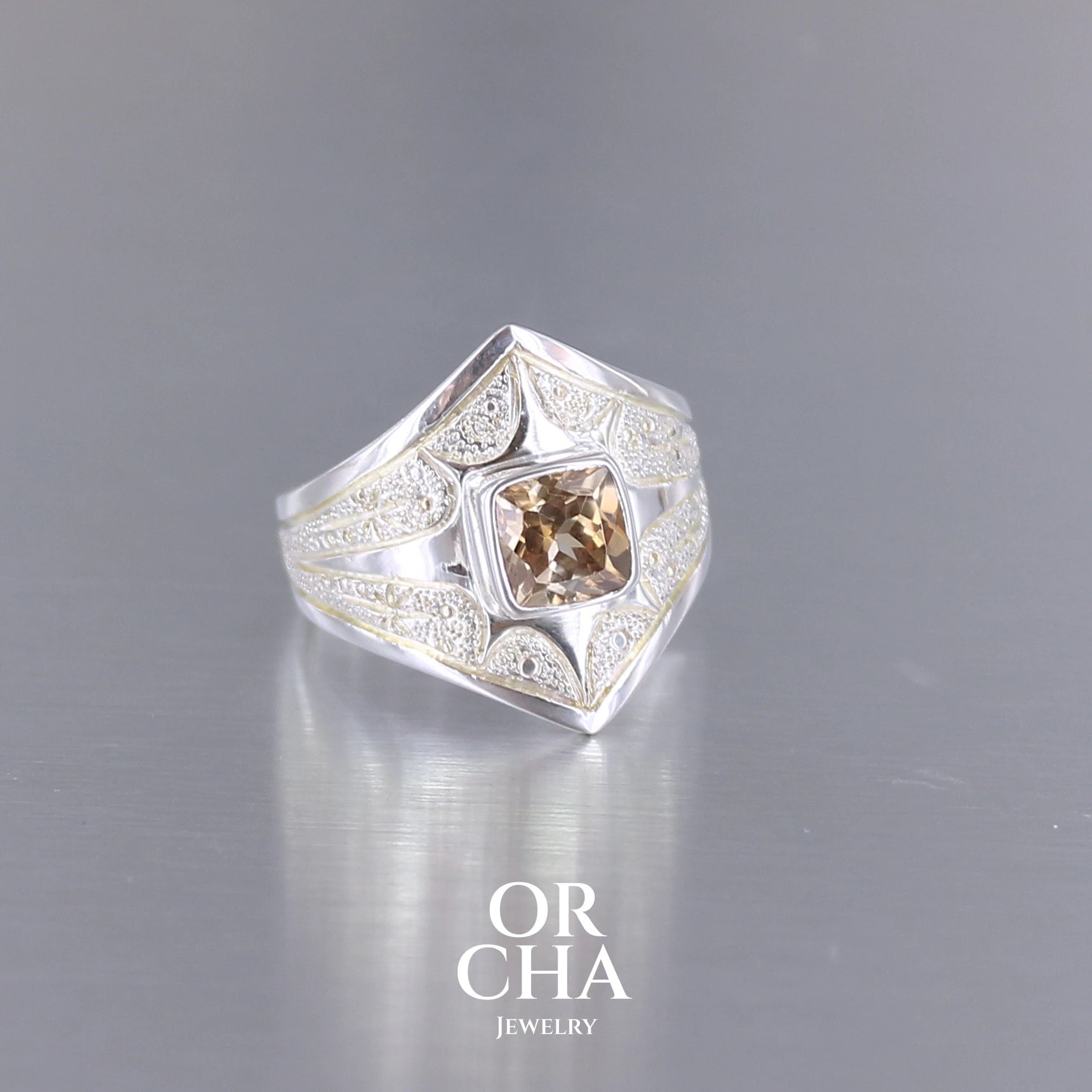 Profil d'une bague pour femme en argent massif sculptées d'étoiles et autres corps célestes sertie d'une Topaze dorée aux nuances colorées de dorées à bruns. Pierre naturelle, facettée de forme carrée, de qualité transparente présentant un très bel éclat. Taille 55. Bijoux unique, éthique et durable présenté dans un coffret de notre marque, prêt à offrir. Livraison offerte, certificat d'authenticité, service client.