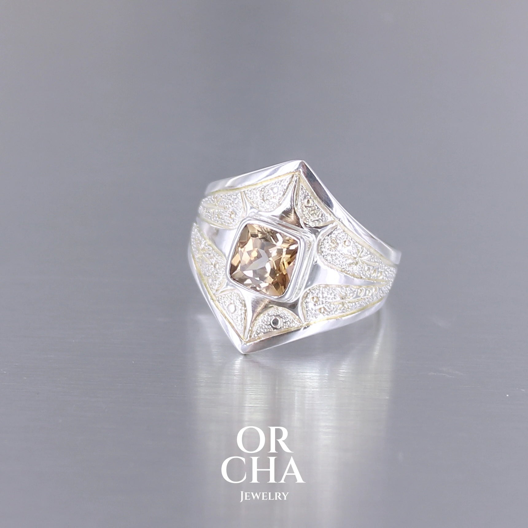 Profil d'une bague pour femme en argent massif sculptées d'étoiles et autres corps célestes sertie d'une Topaze dorée aux nuances colorées de dorées à bruns. Pierre naturelle, facettée de forme carrée, de qualité transparente présentant un très bel éclat. Taille 55. Bijoux unique, éthique et durable présenté dans un coffret de notre marque, prêt à offrir. Livraison offerte, certificat d'authenticité, service client.