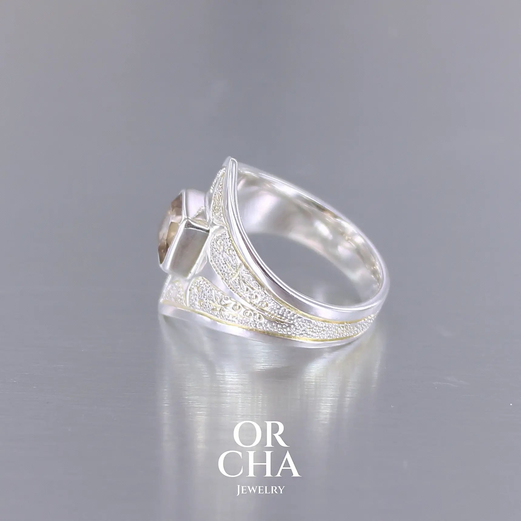 Profil d'une bague pour femme en argent massif sculptées d'étoiles et autres corps célestes sertie d'une Topaze dorée aux nuances colorées de dorées à bruns. Pierre naturelle, facettée de forme carrée, de qualité transparente présentant un très bel éclat. Taille 55. Bijoux unique, éthique et durable présenté dans un coffret de notre marque, prêt à offrir. Livraison offerte, certificat d'authenticité, service client.